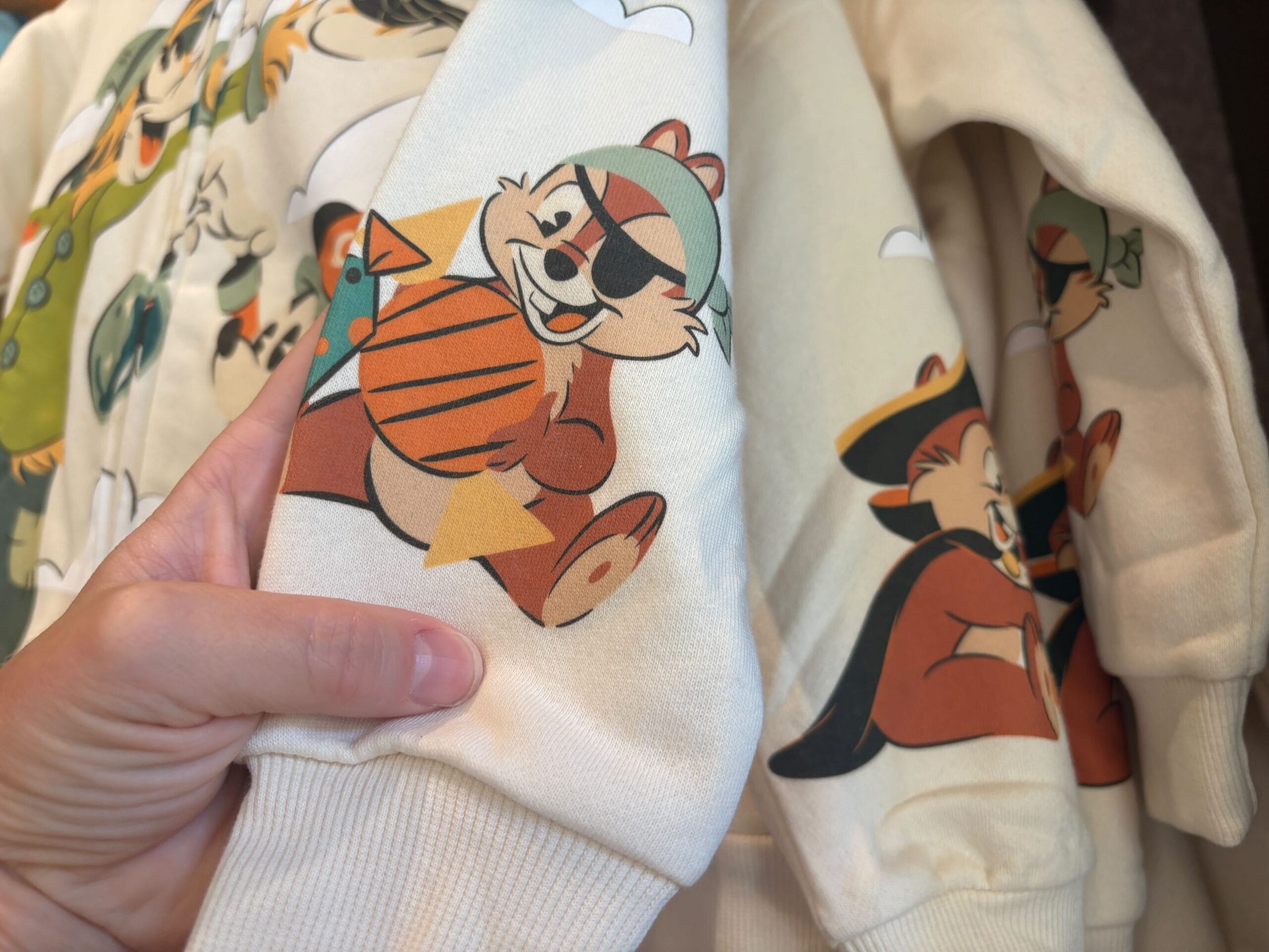 A hand holds a hoodie with cartoon chipmunks in pirate gear, part of the Halloween merchandise at Walt Disney World.
