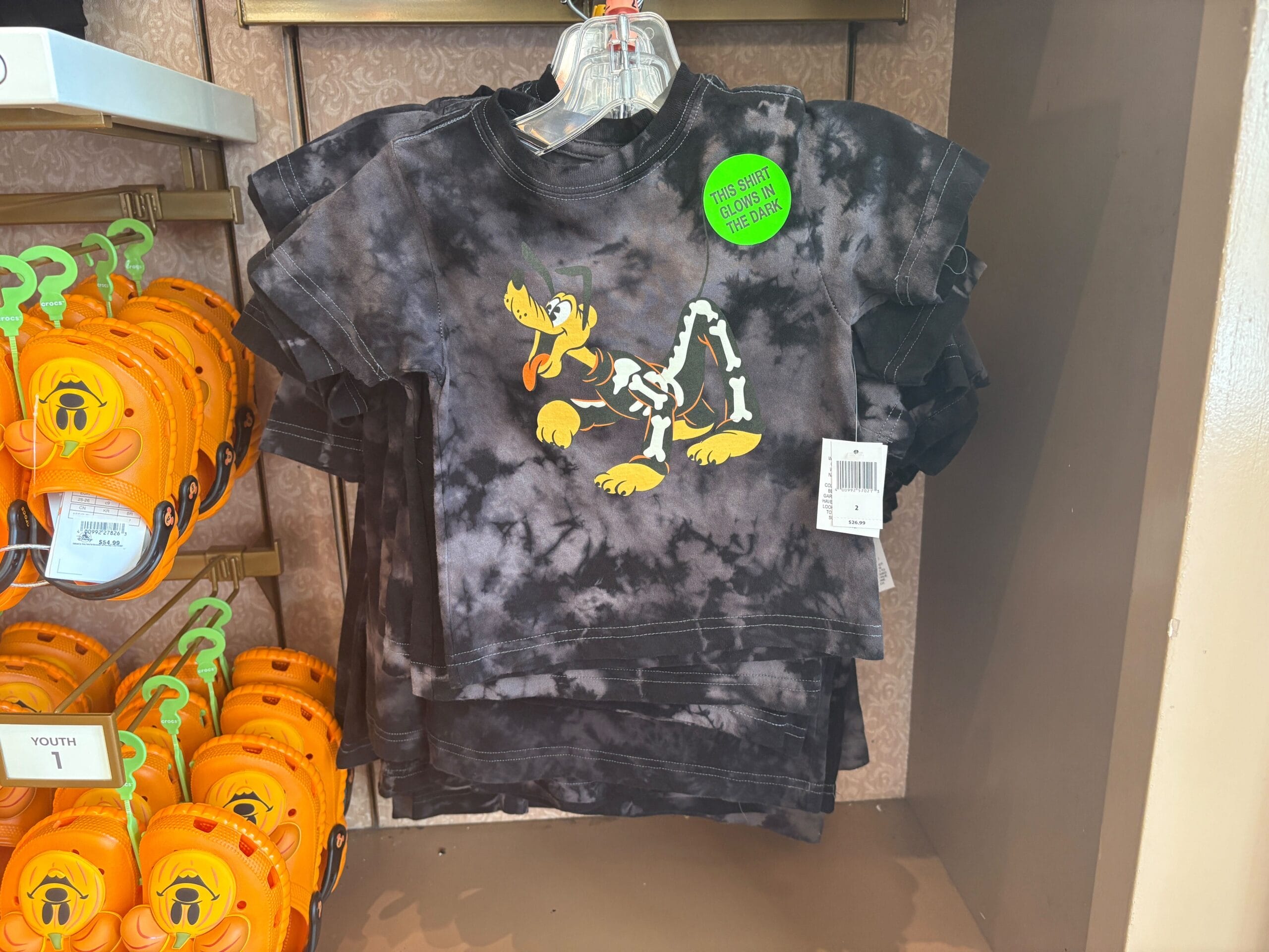Black tie-dye kids’ shirt with a cartoon dog skeleton graphic, perfect as Halloween merchandise on display.