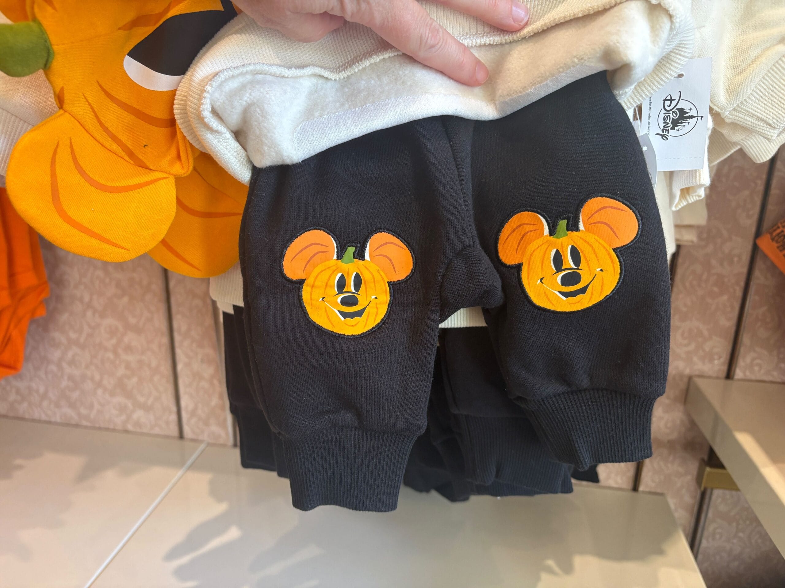 Black pants for children with Mickey-shaped pumpkin faces, part of Walt Disney World Halloween merchandise on display.