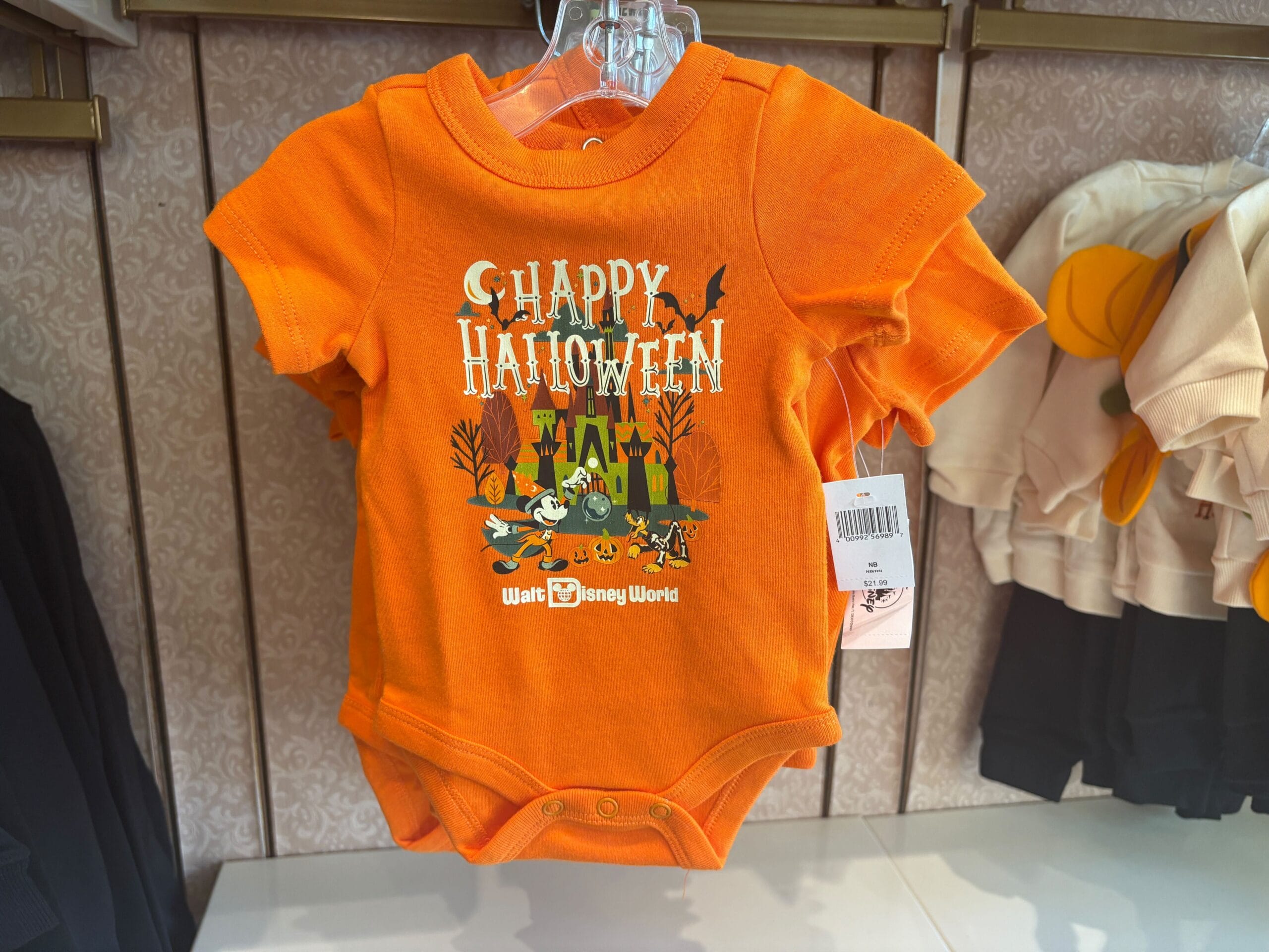 Disney Halloween Merch 2025 - Orange baby onesie with "Happy Halloween" and Disney characters, part of Walt Disney World Halloween merchandise in-store.