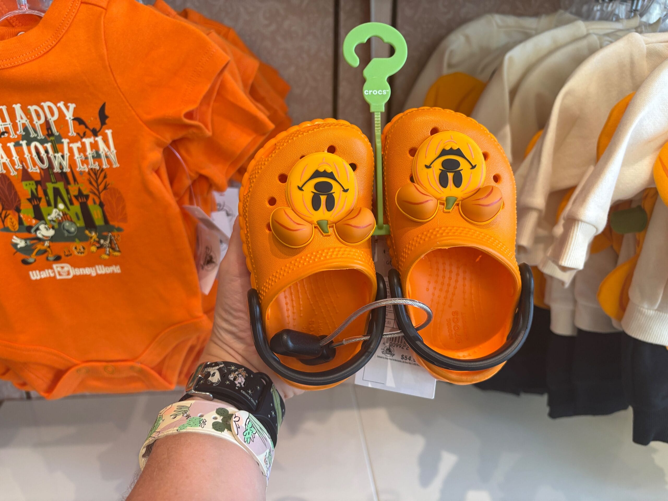 A hand holds orange Crocs with a Pluto face in front of Walt Disney World Halloween merchandise.