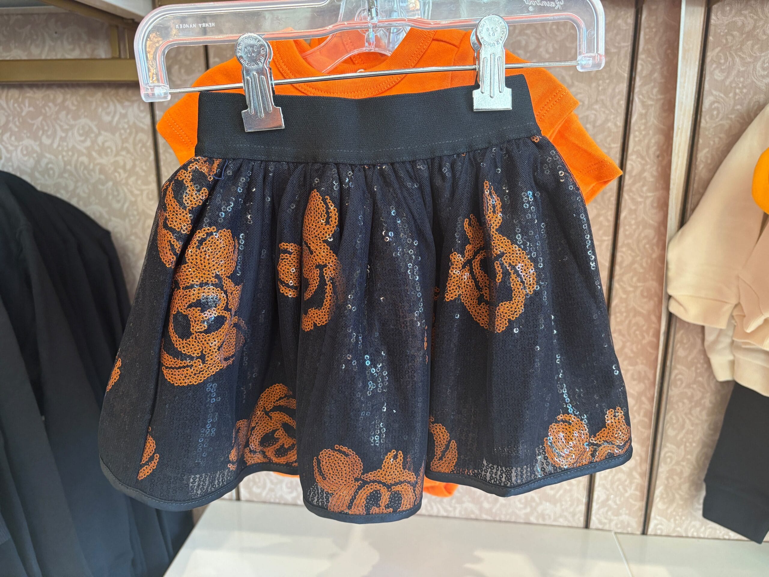 Black mesh skirt with orange sequin pumpkins, part of the Halloween merchandise, displayed over an orange shirt.