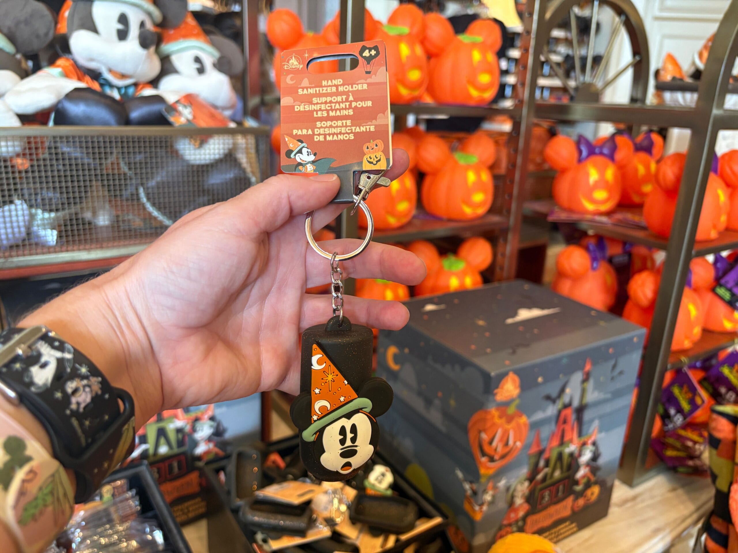A hand holds a Halloween-themed Mickey Mouse keychain among Walt Disney World Halloween merchandise and pumpkin decor.