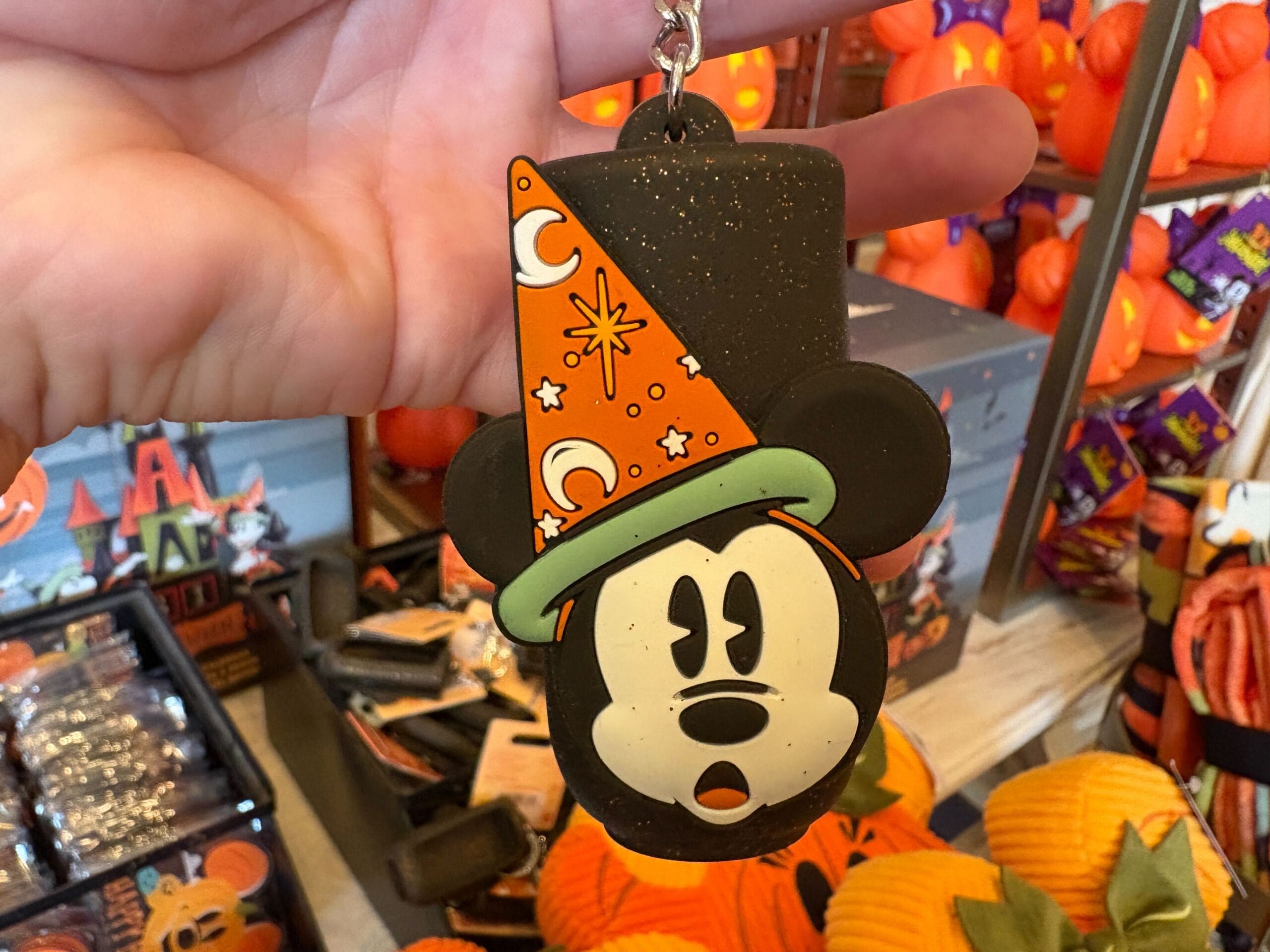 A hand holds Walt Disney World Halloween merchandise—Mickey Mouse in an orange wizard hat—in a festive store display.