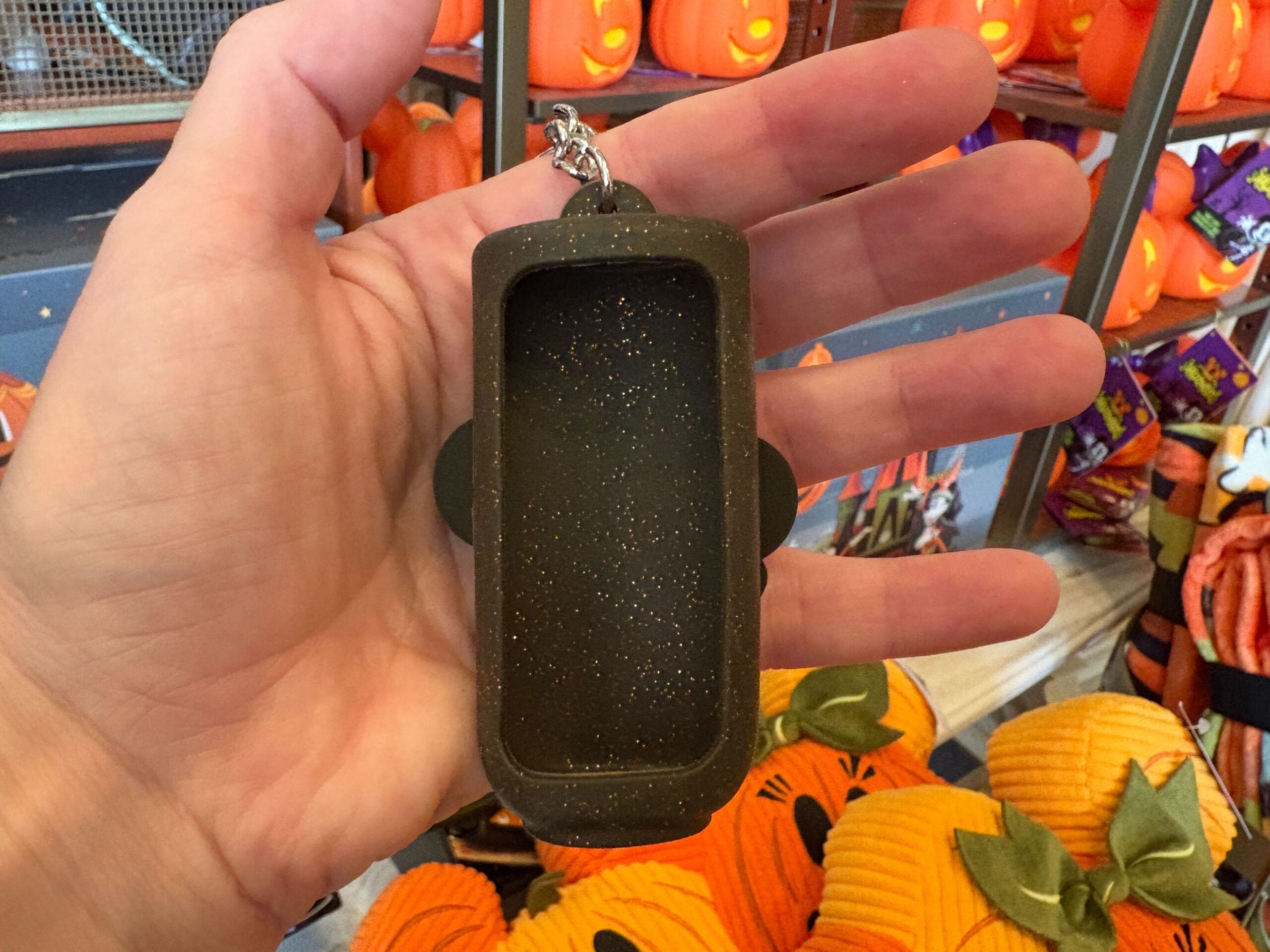 A hand holds an empty, glittery black keychain case among Halloween merchandise at Walt Disney World.
