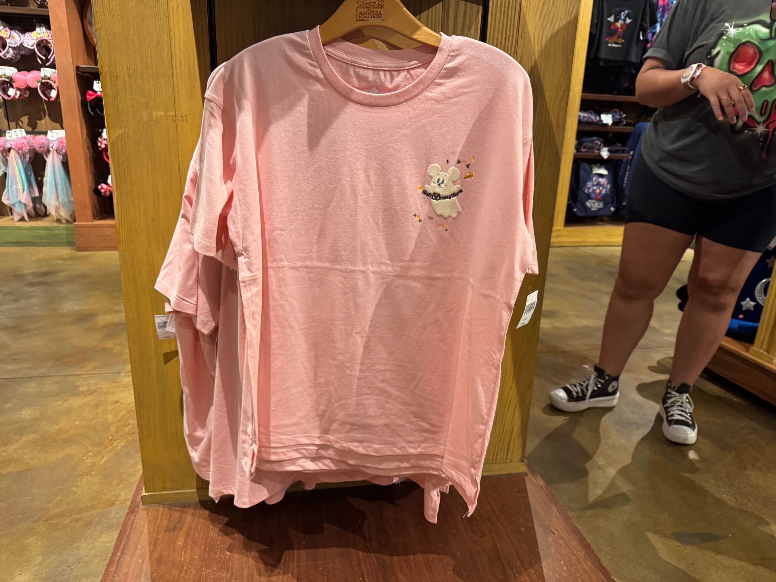 Light pink T-shirt with Figment the dragon, part of Walt Disney World merchandise, displayed on a wooden rack in-store.