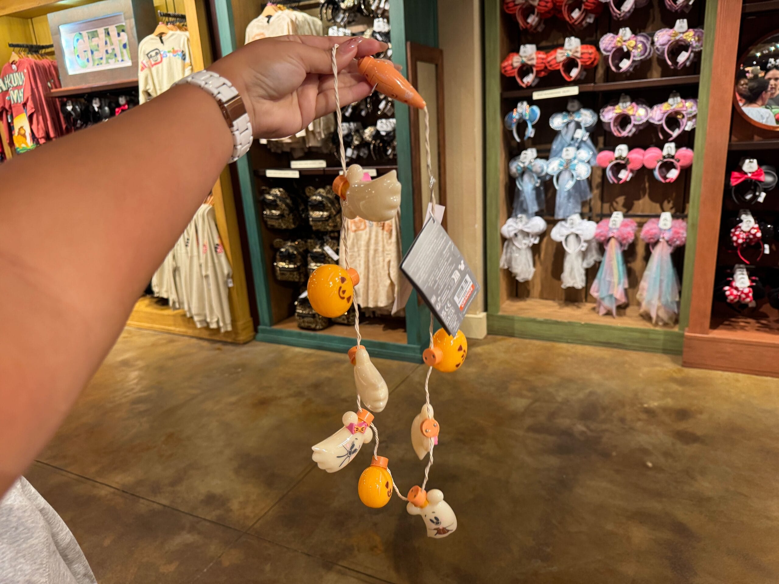 A hand holds chicken and egg ornaments in a Walt Disney World store filled with Disney merchandise and Minnie Mouse ears.