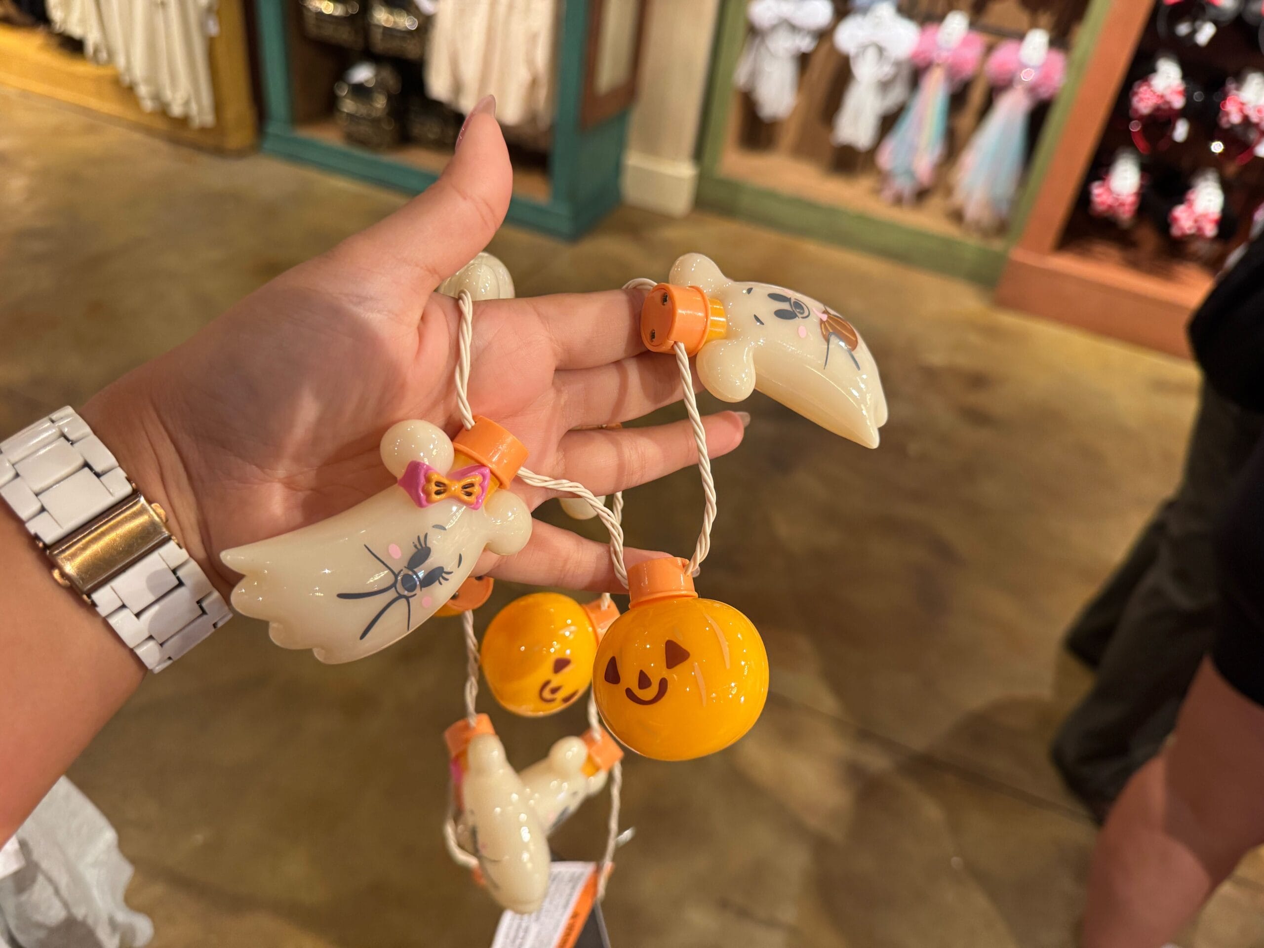 A hand holds a string of cute ghost and pumpkin Halloween merchandise lights in a store.