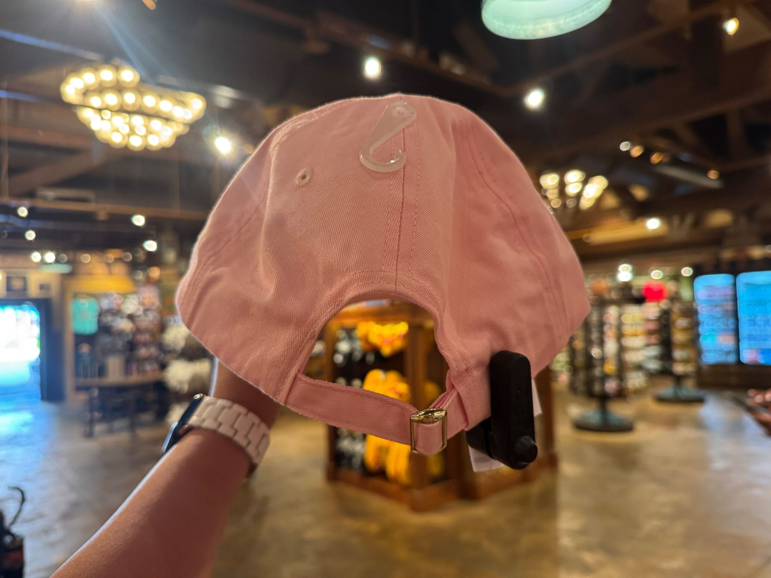 Person holding a pink baseball cap with a security tag in a store, prices and shelves blurred in the background.