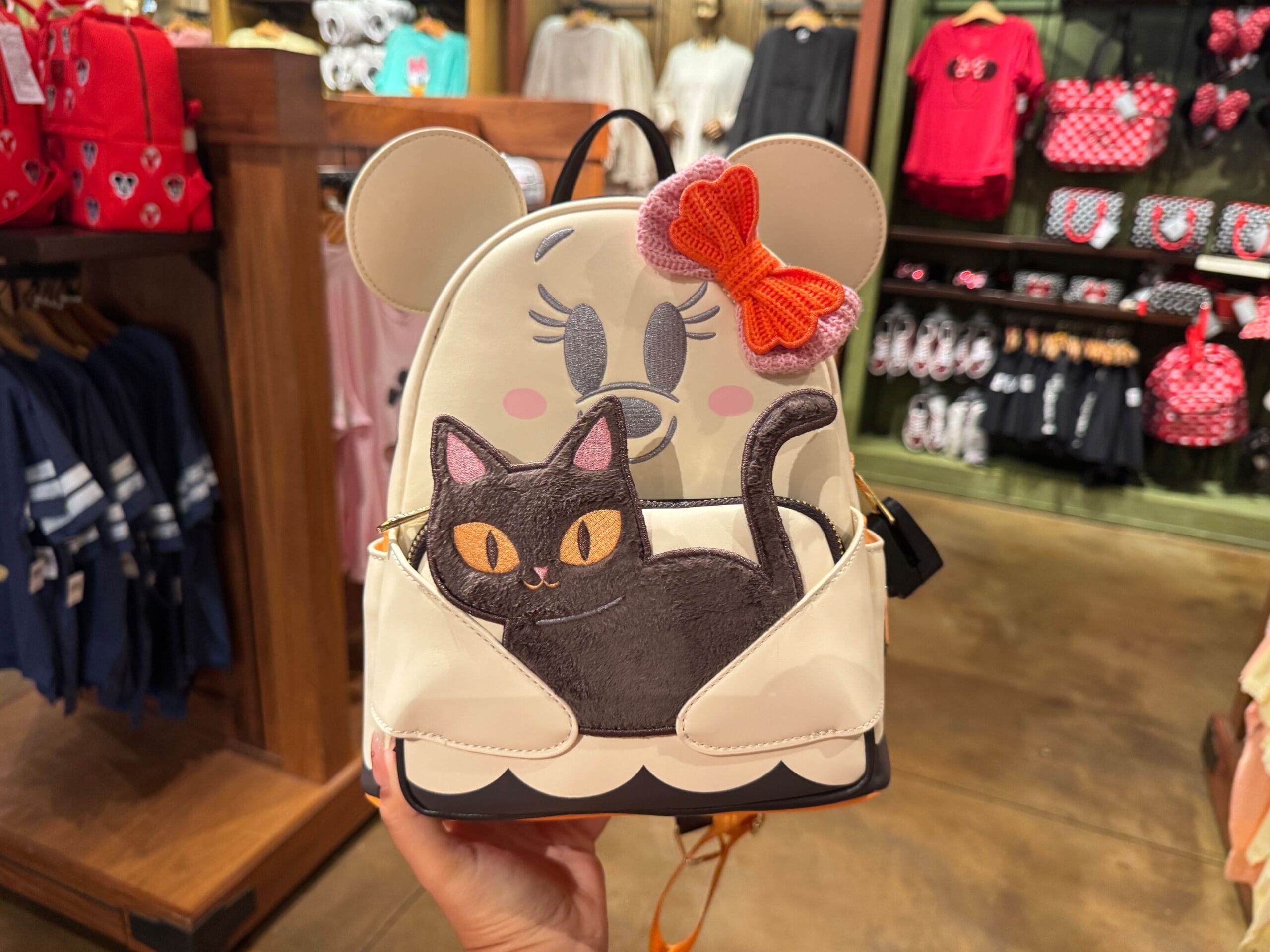 A hand holds a Minnie Mouse backpack with a black cat, spotted among Walt Disney World Halloween merchandise in-store.