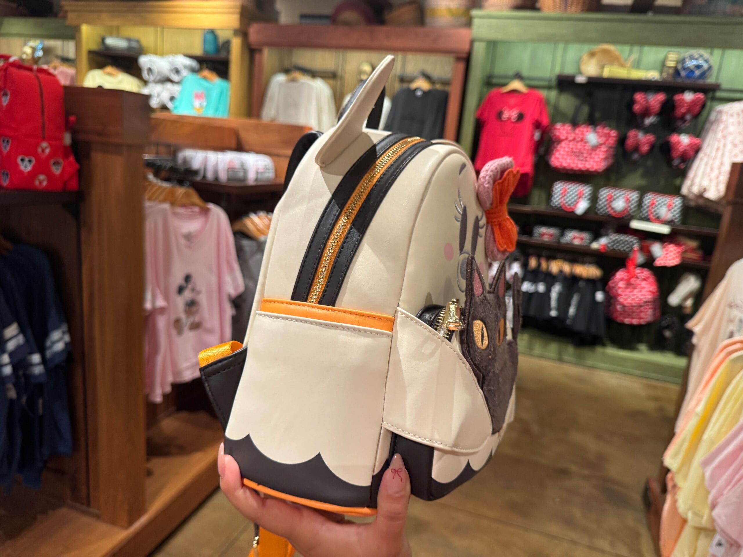 A person holds a small animal-themed backpack among colorful Walt Disney World bags and clothing in the store.