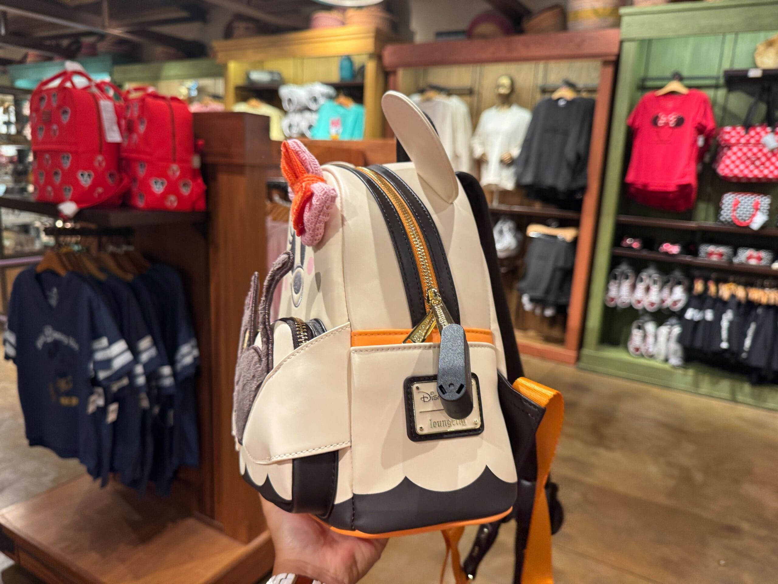 A hand holds a white owl-themed backpack in a store with colorful Walt Disney World Halloween merchandise on shelves.