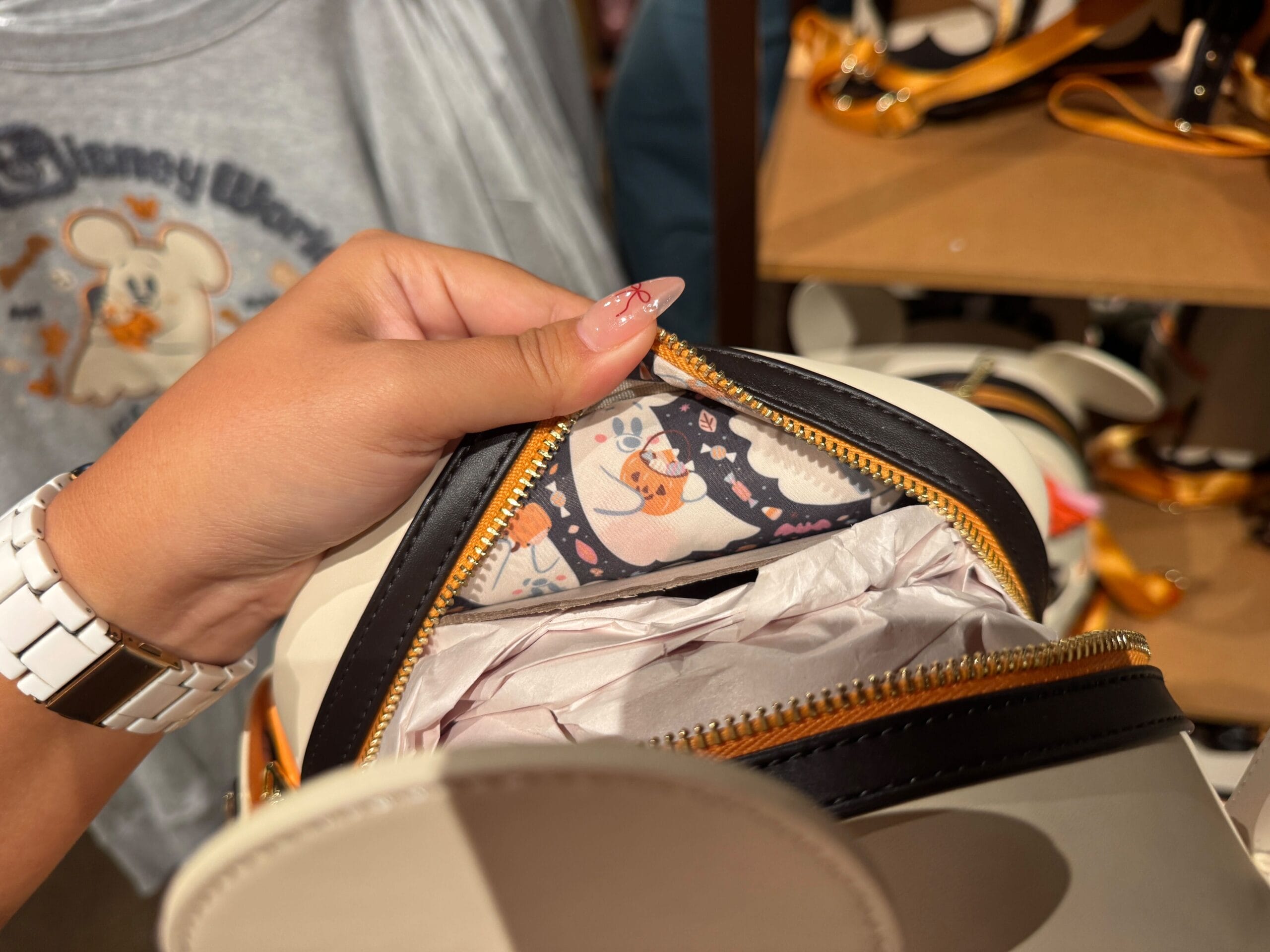 A hand opens a small purse, revealing a cute orange pumpkin print lining—perfect for Halloween merchandise lovers.
