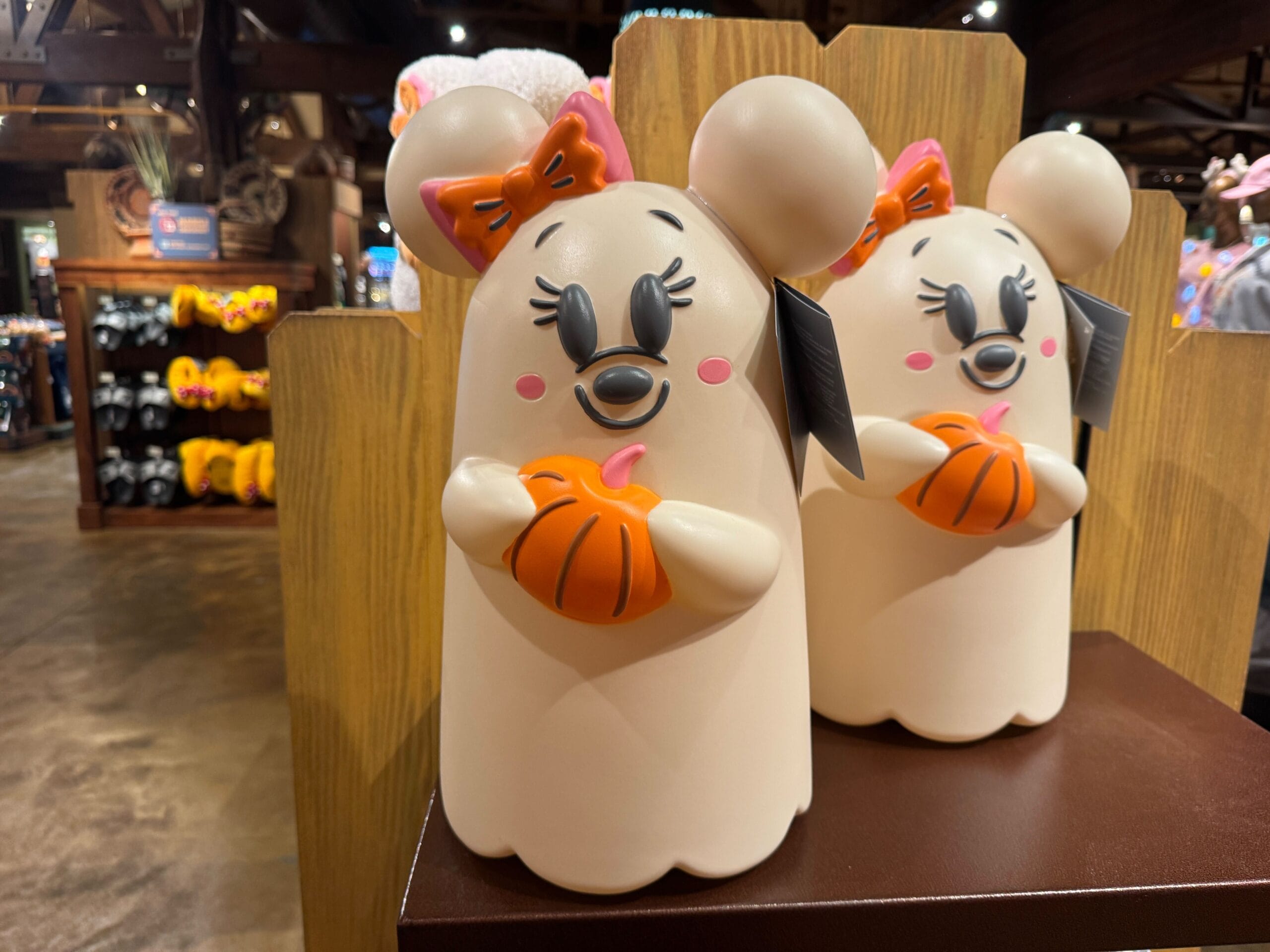 Two Minnie Mouse ghost figurines holding pumpkins sit on a shelf among Walt Disney World Halloween merchandise.