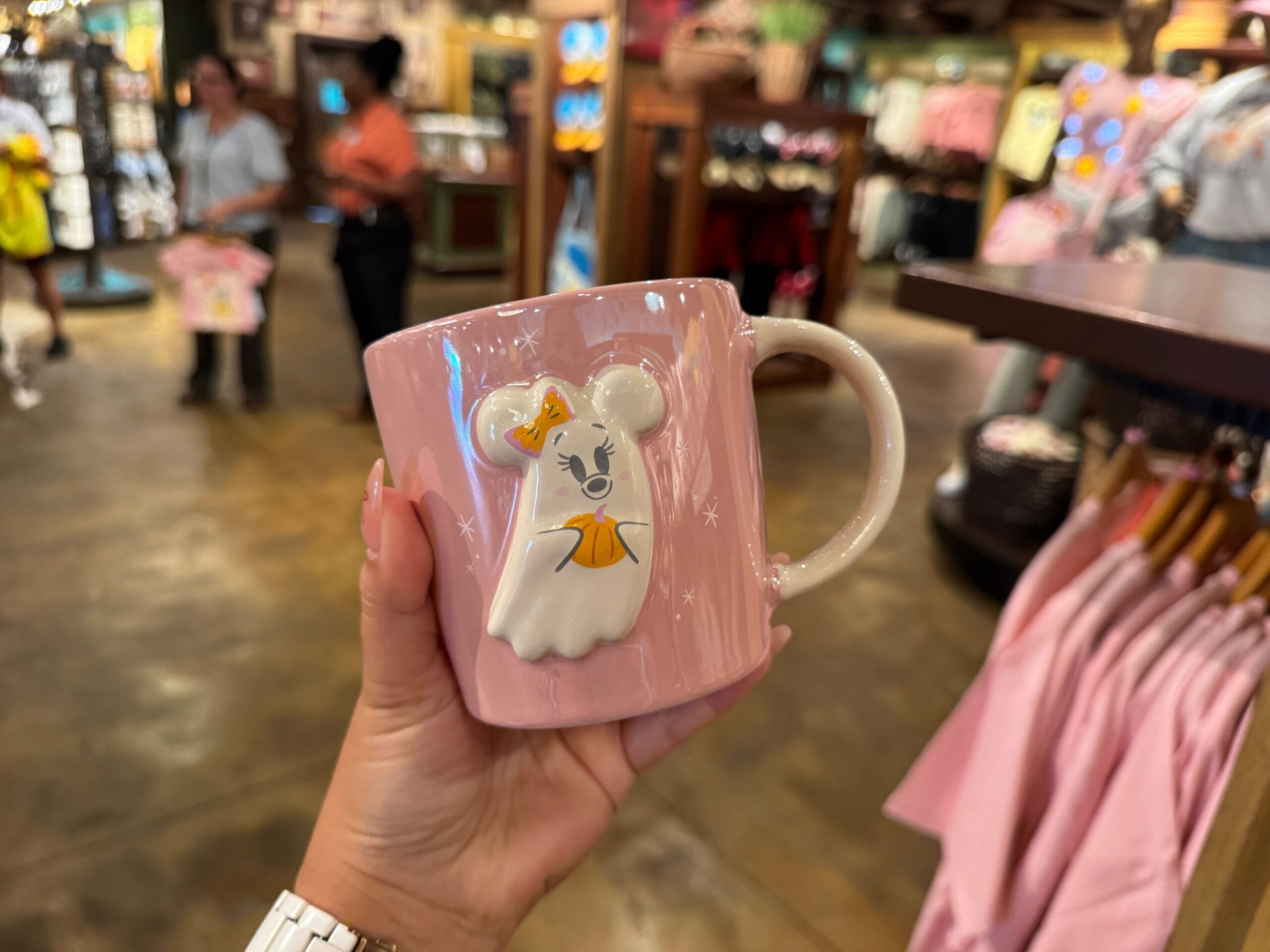 A hand holds a pink Minnie Mouse ghost mug, a cute piece of Halloween Merchandise at Walt Disney World.