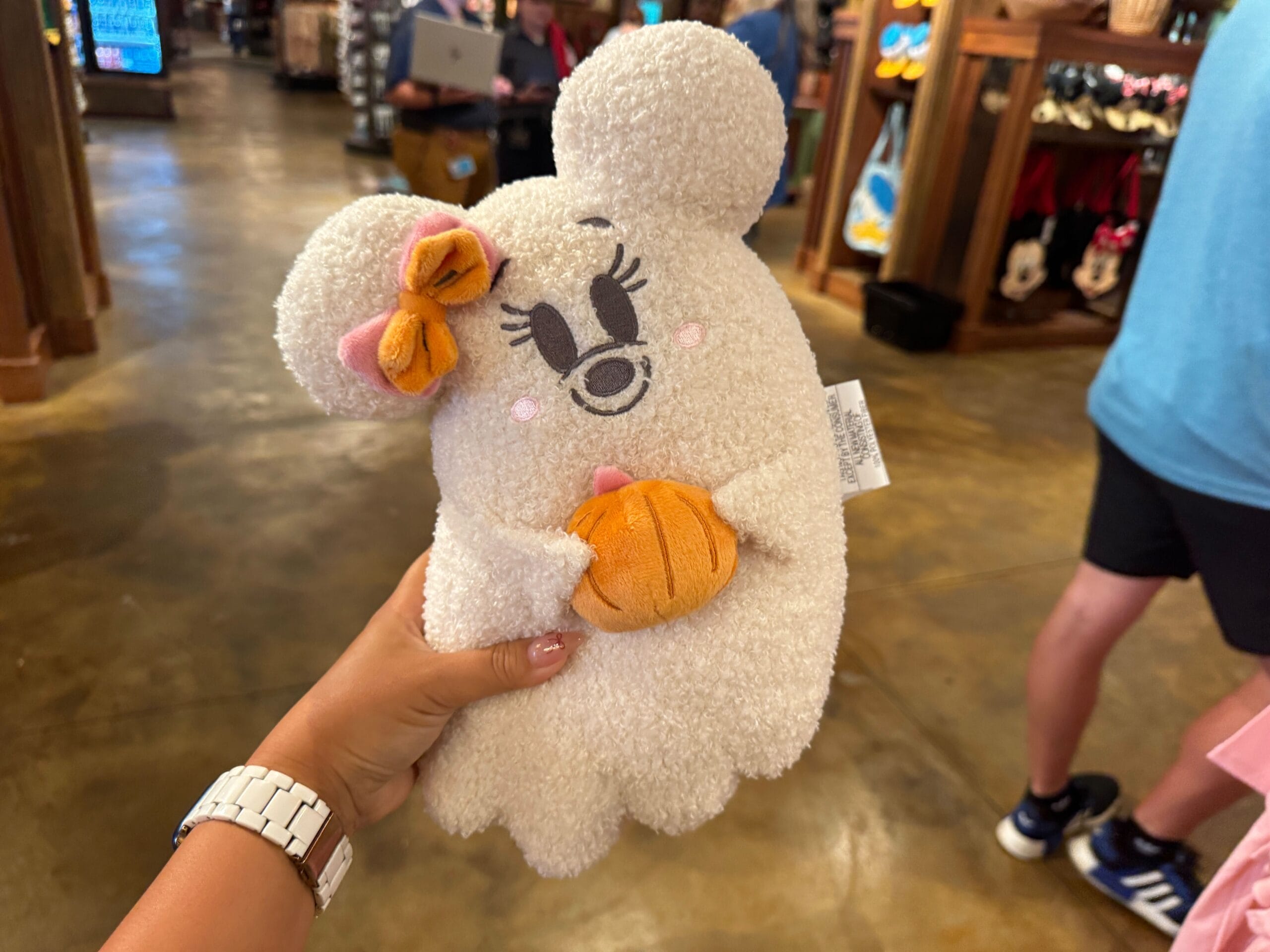 A hand holds a plush Minnie Mouse ghost with a bow and pumpkin, part of Walt Disney World Halloween merchandise in-store.