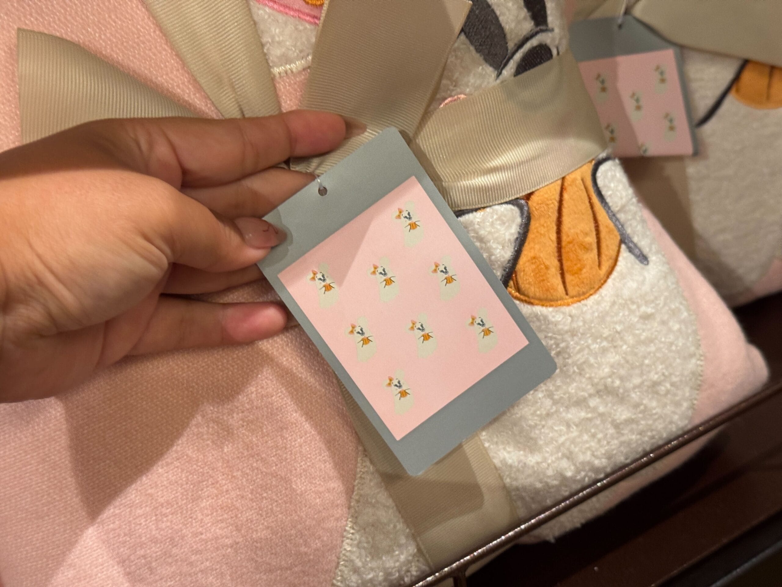 A hand holds a gift tag with small flowers, attached to pastel fabric—perfect for Walt Disney World Halloween merchandise.