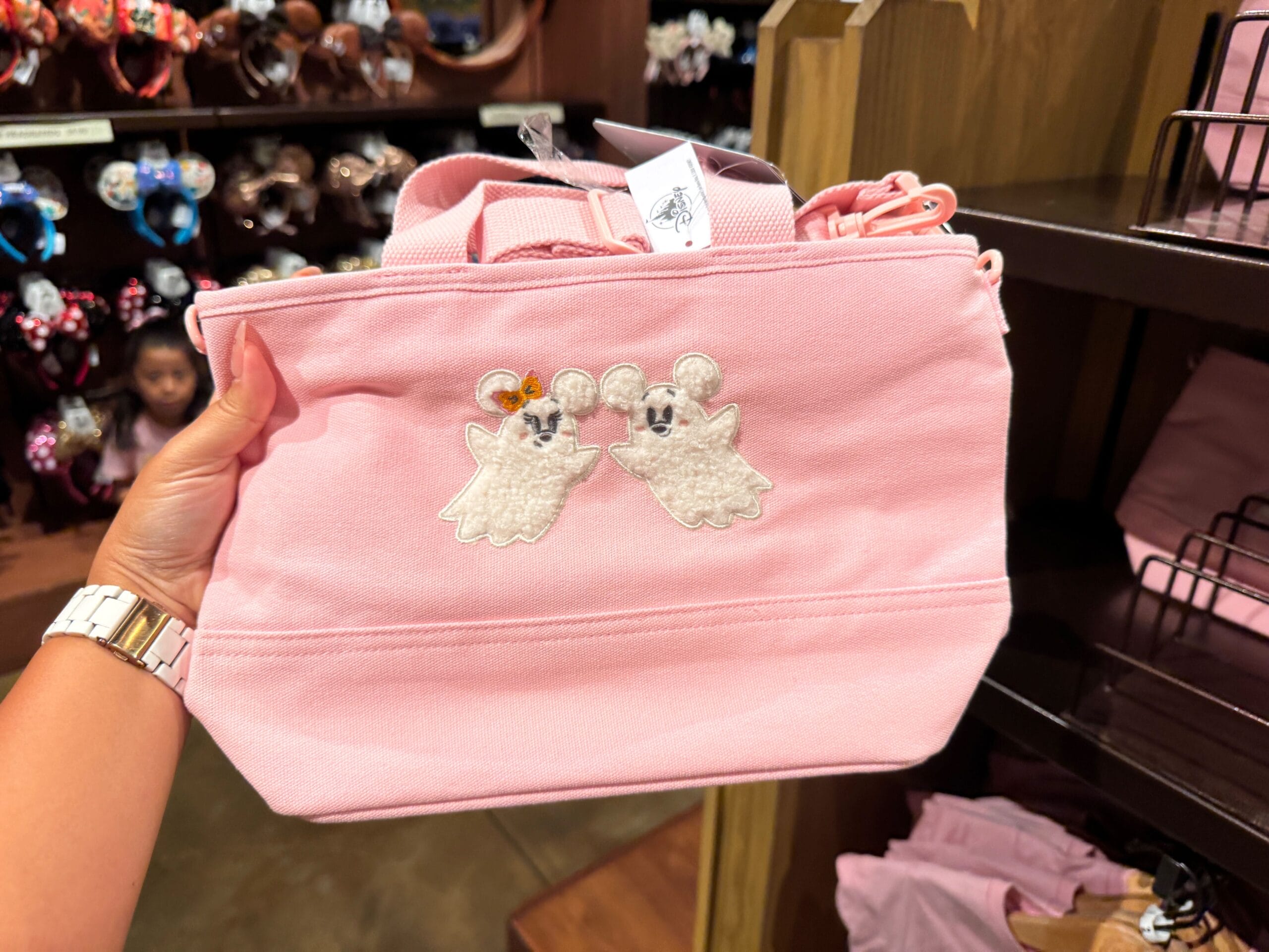 A hand holds a pink tote bag with embroidered ghost mice, part of cute Halloween merchandise at Walt Disney World.