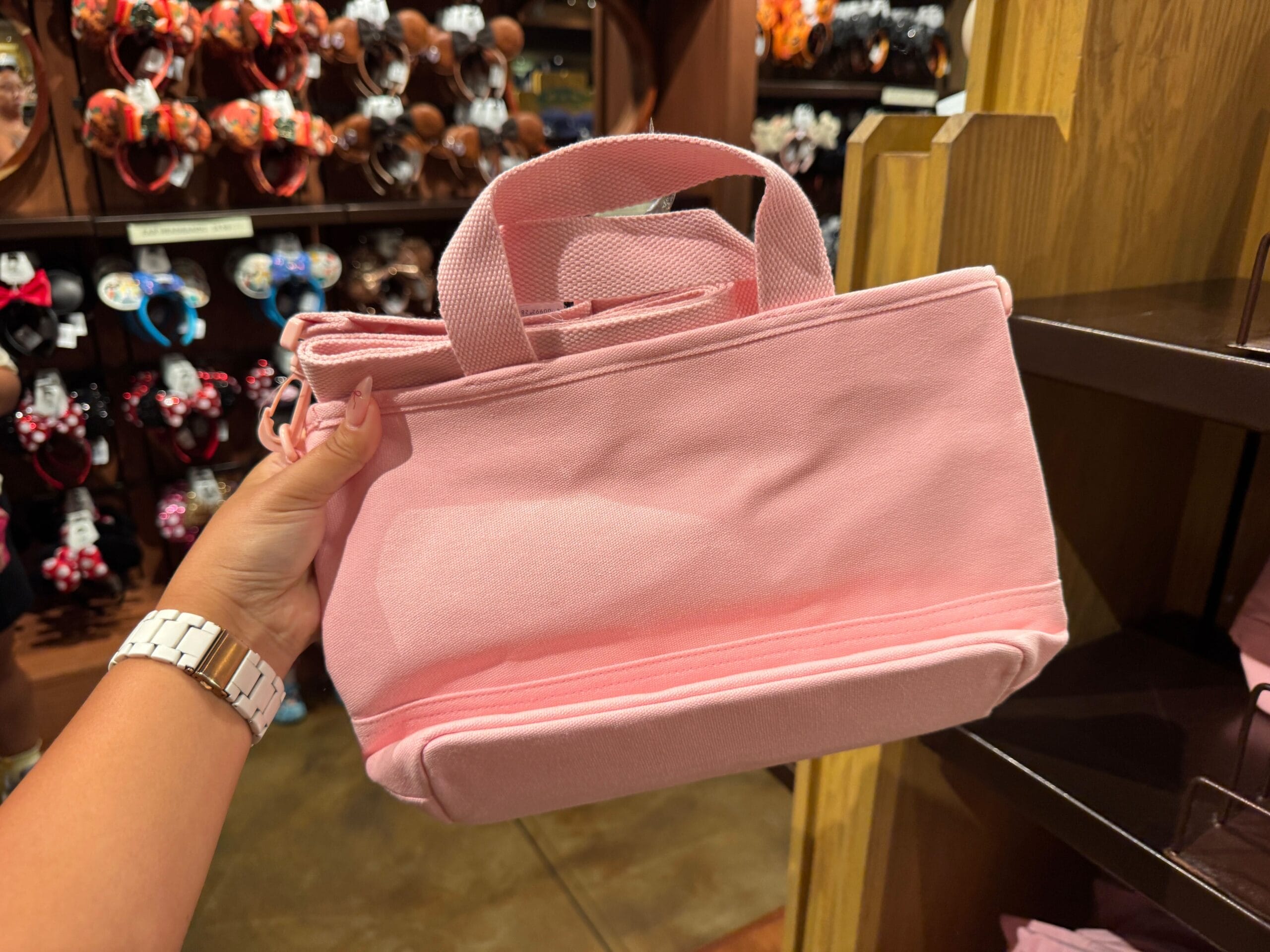 A hand holds a light pink tote bag in a store filled with colorful Halloween merchandise at Walt Disney World.