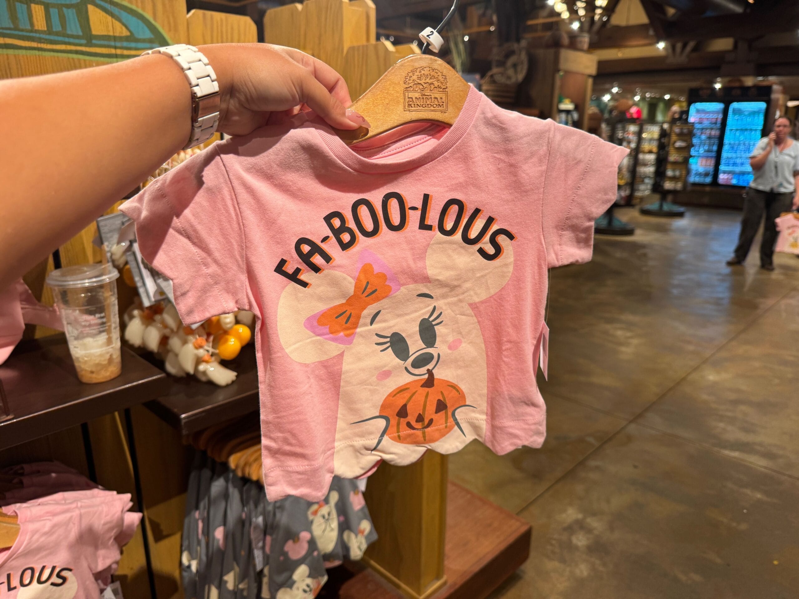 A hand holds a pink toddler shirt with a mouse and "Fa-BOO-lous" text, part of Walt Disney World Halloween merchandise.