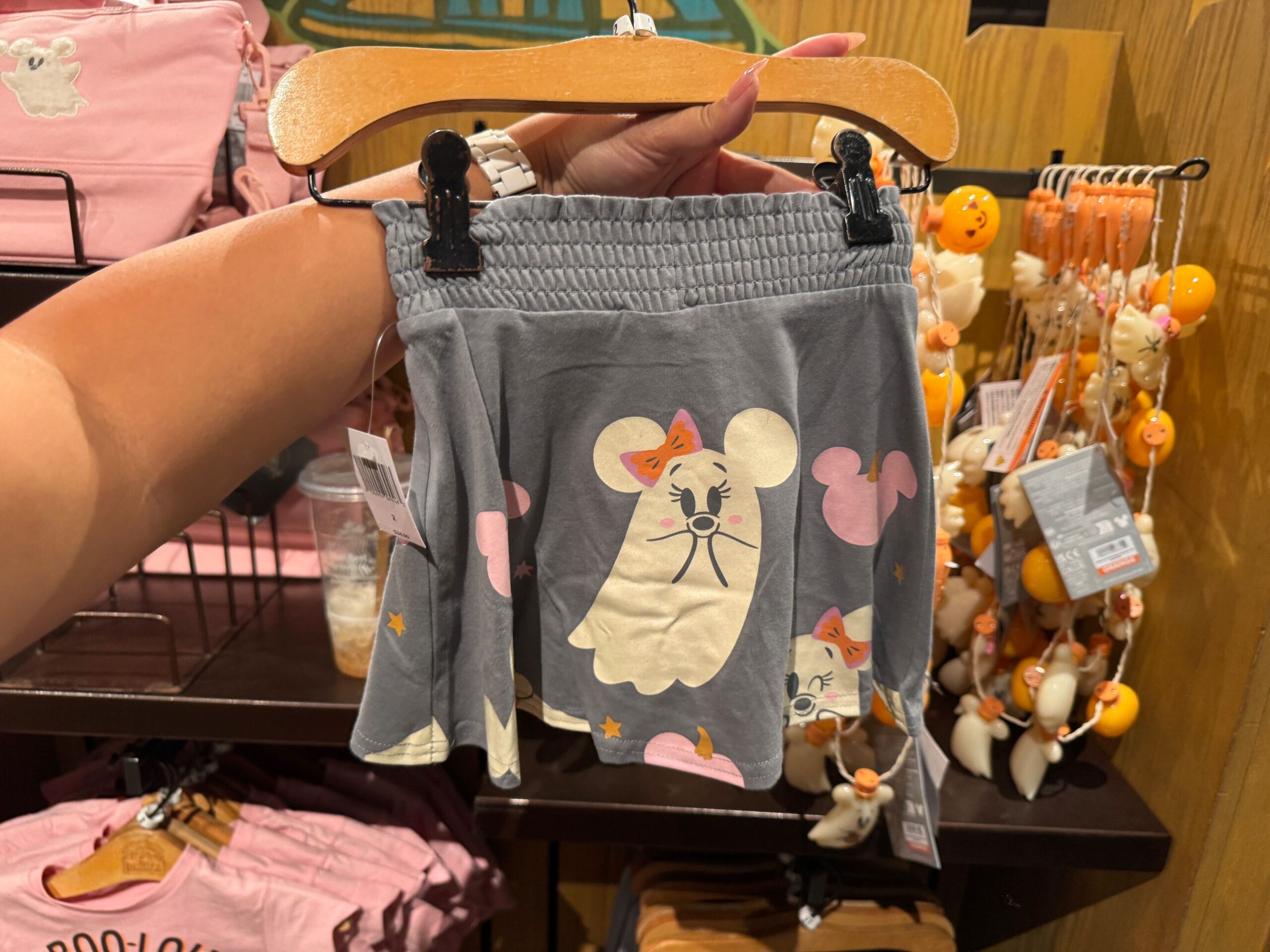 Gray children's skirt with a ghost mouse face print, part of the Halloween merchandise display in store with pink bags.