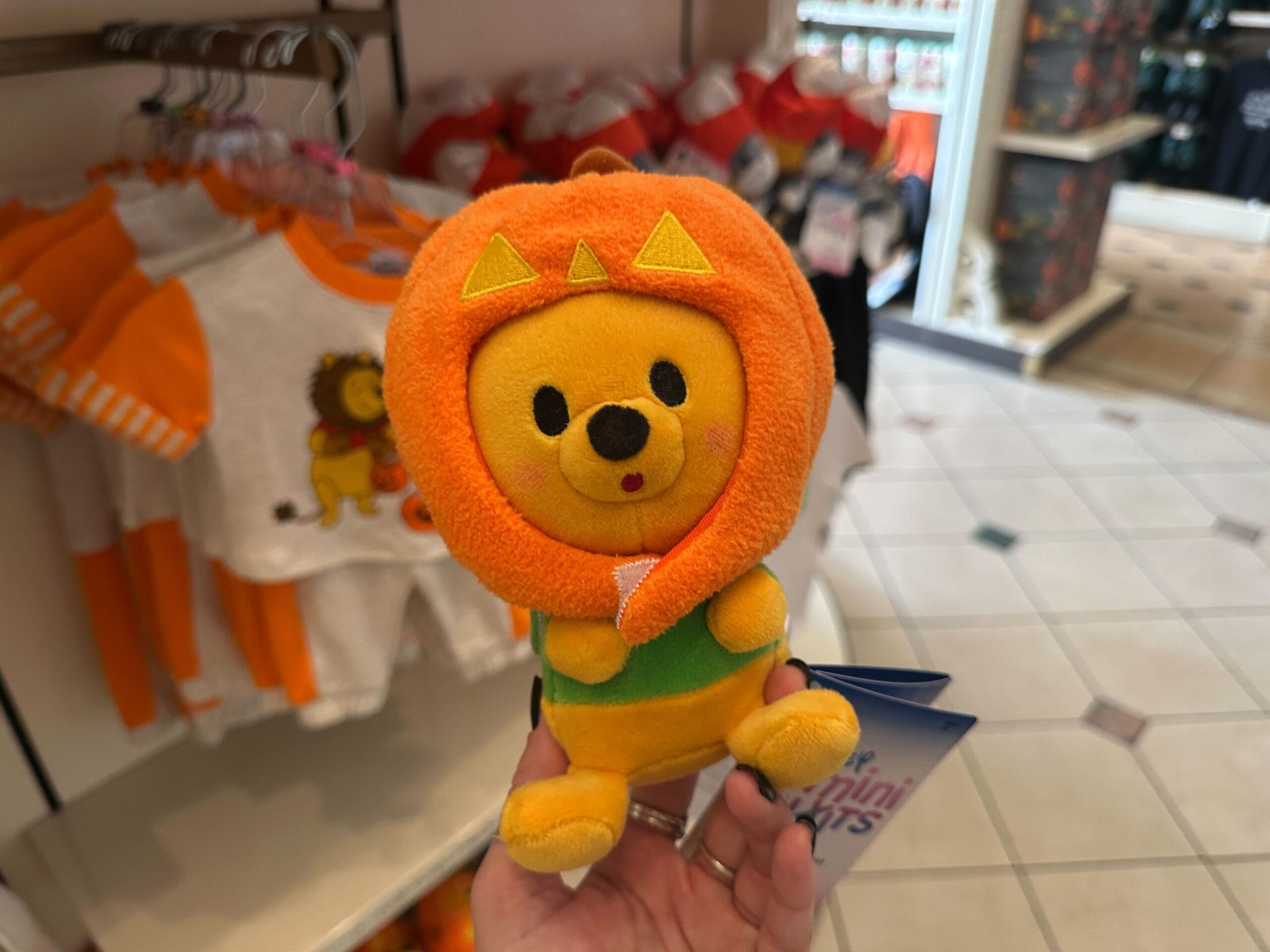 A plush bear toy in a lion mane costume is held in-store, part of Disney Halloween Merch 2025 at Walt Disney World.