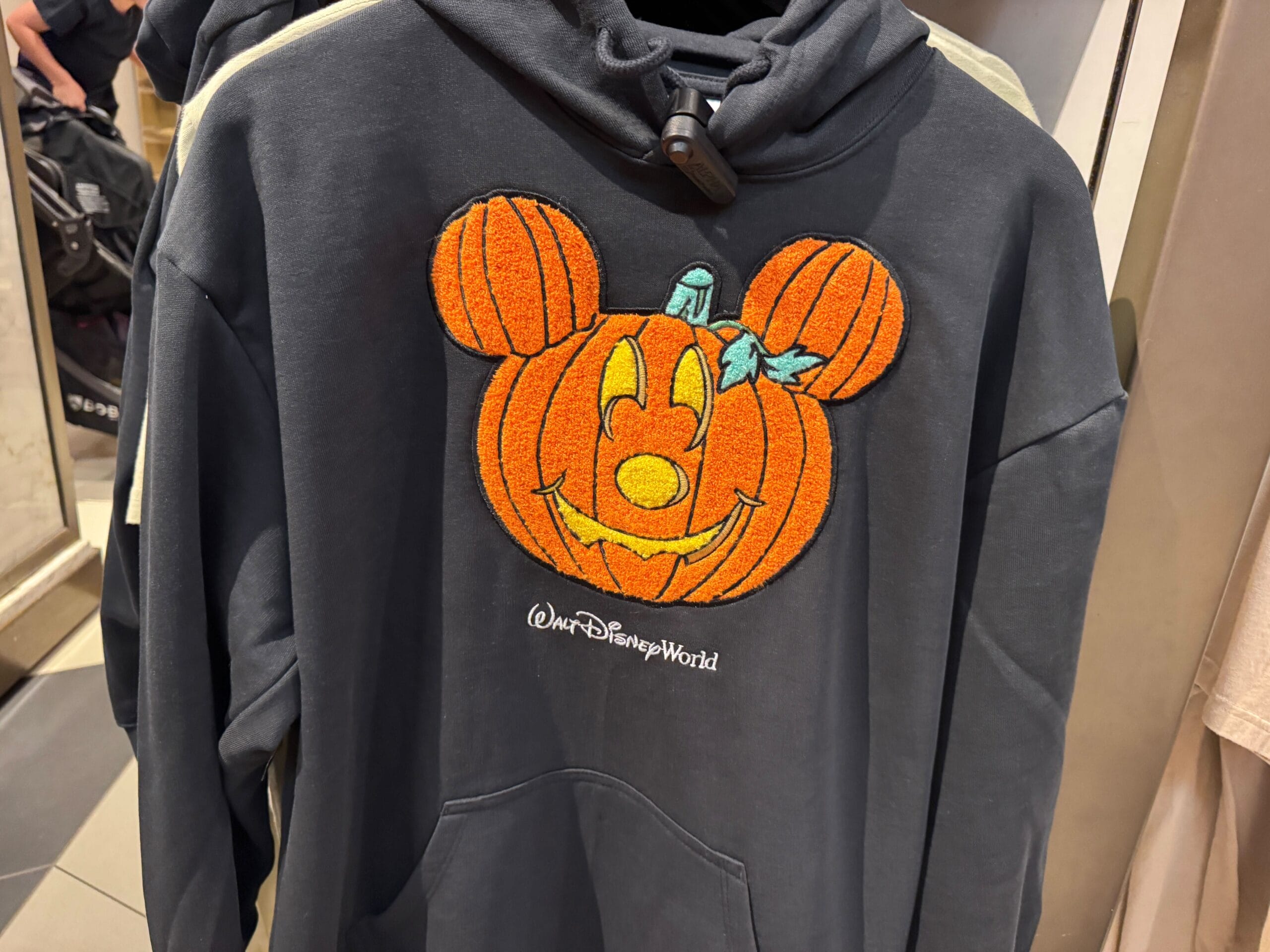 A black hoodie featuring a Mickey Mouse pumpkin and "Walt Disney World," ideal 2025 Halloween merch—distinct from Disneyland styles.