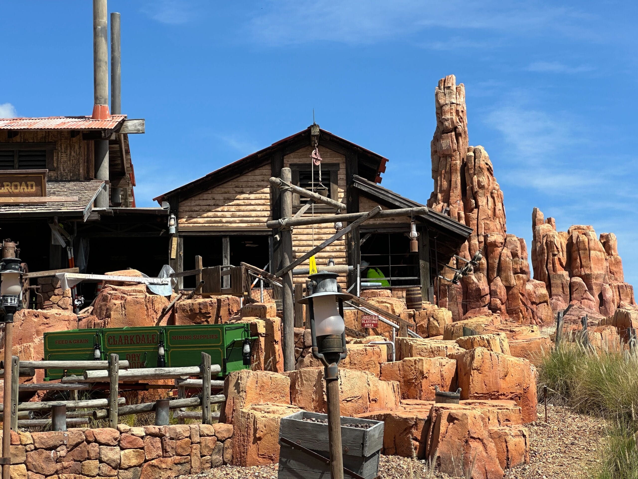 A rustic wooden building and railroad tracks set among red rock formations under a clear blue sky.
