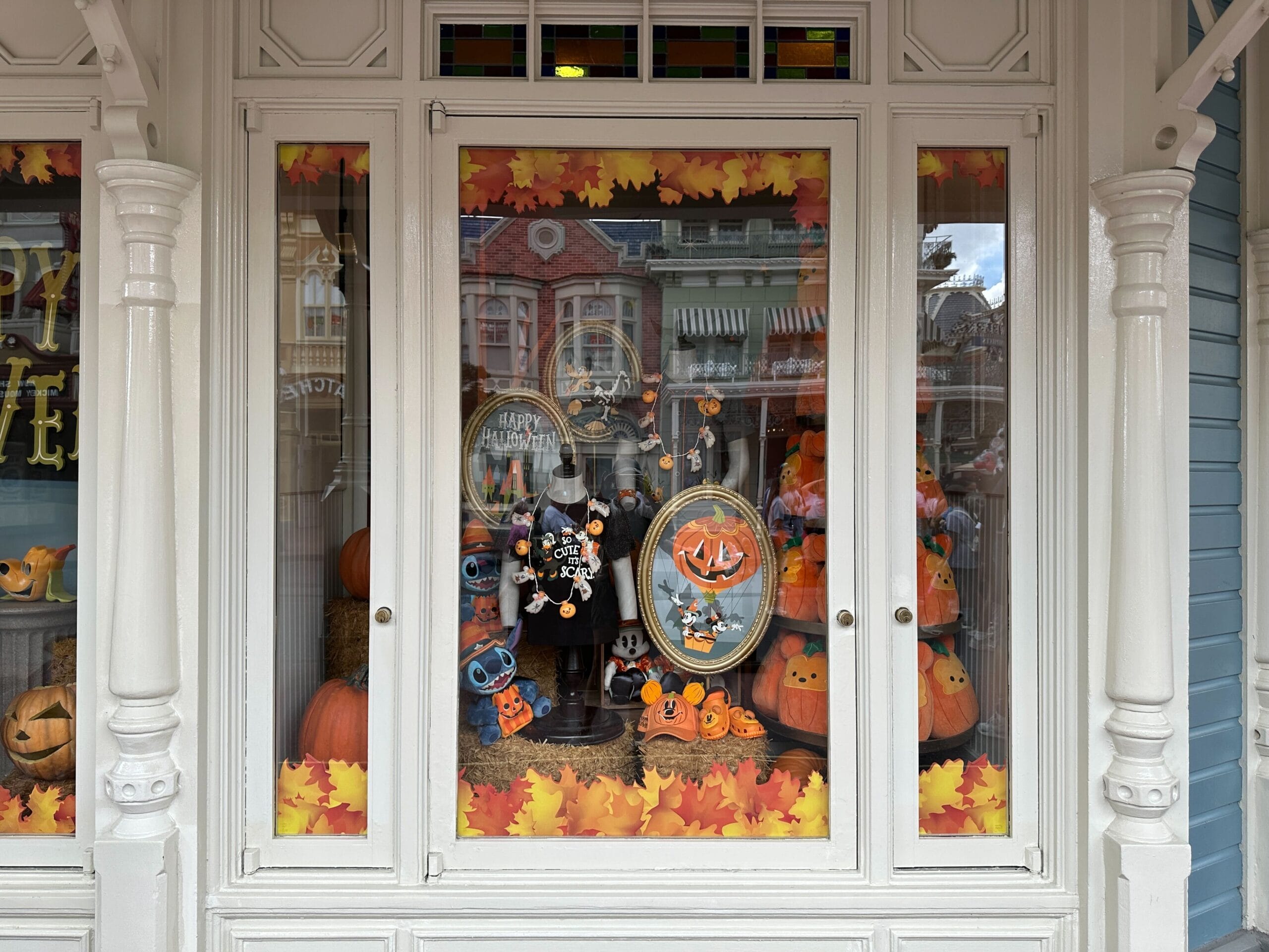 Shop window decorated with pumpkins, Halloween plush toys, and autumn leaves, reflecting buildings across the street.