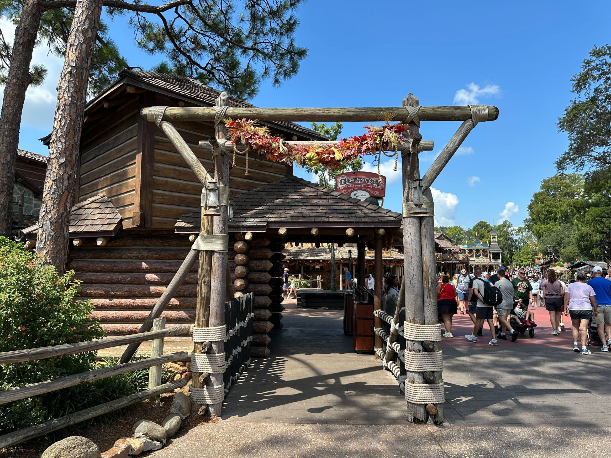 Entrance to a rustic, log cabin-style building with a wooden arch, people walking nearby, and clear blue sky above.