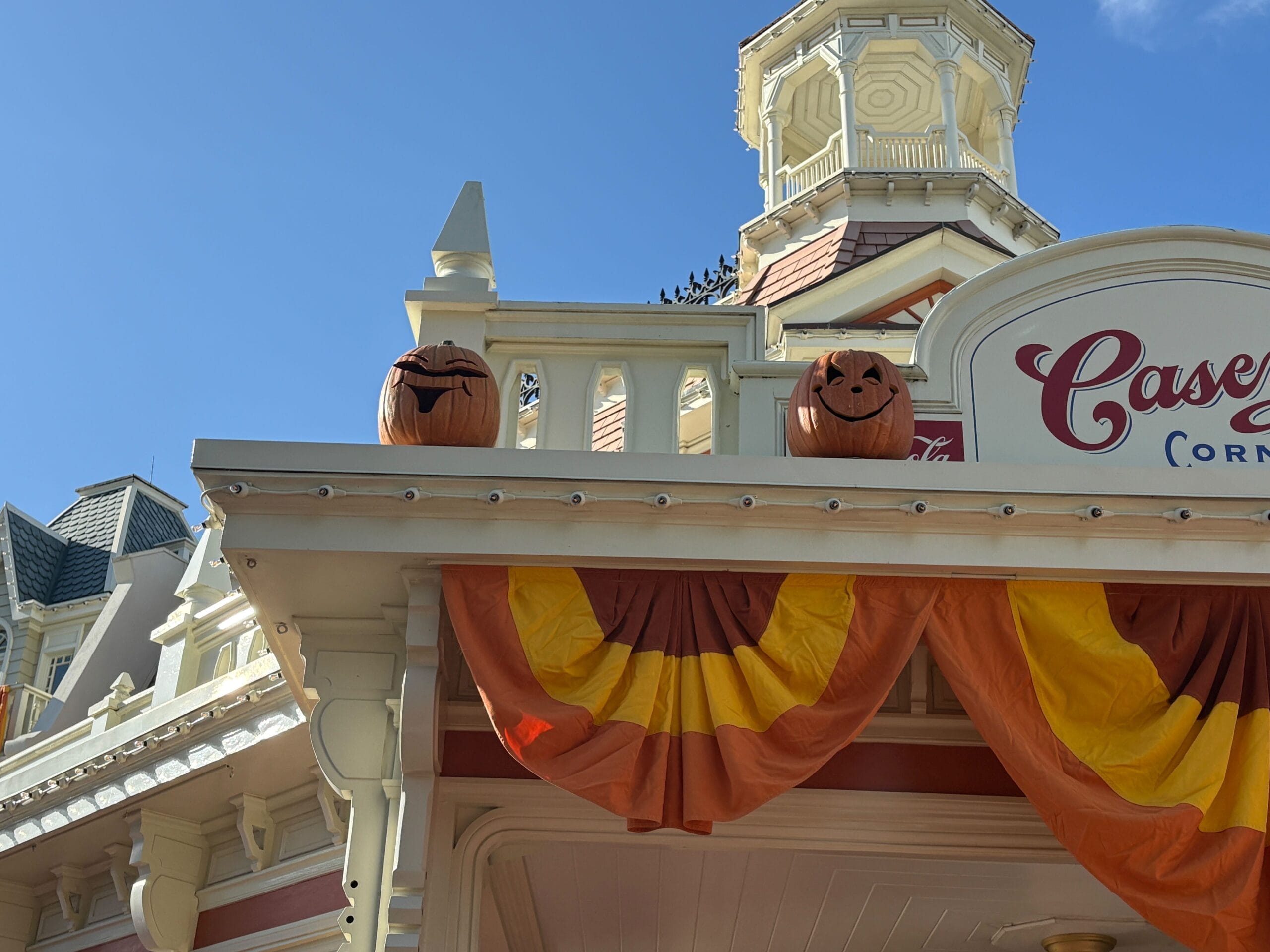 Two Jack-o'-Lanterns and orange-yellow bunting decorate a building under a clear blue sky—classic Halloween decor.