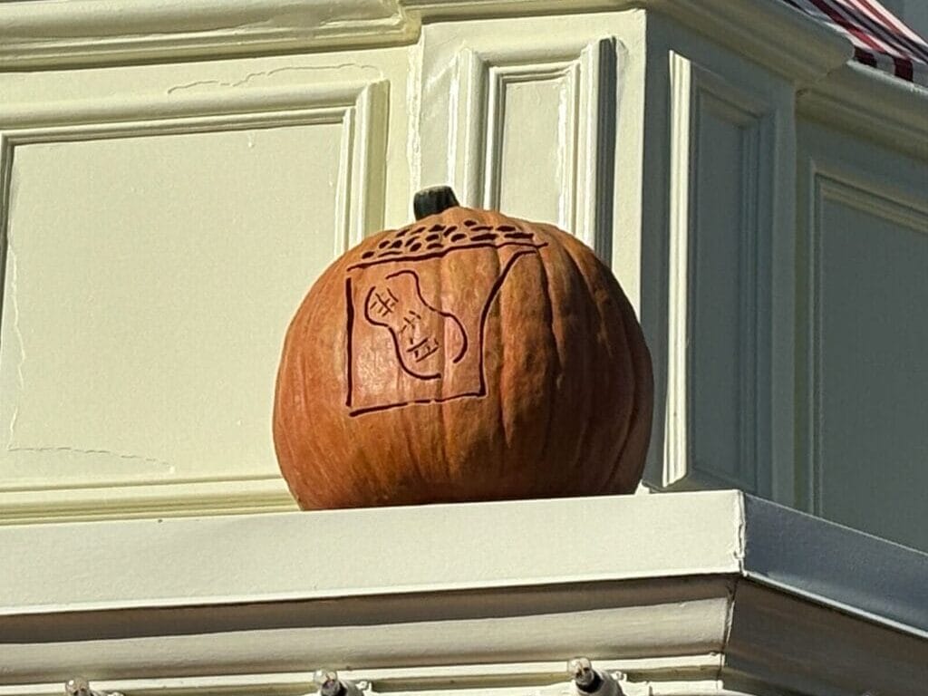 A Mickey Mouse Jack-o'-Lantern sits on a ledge with orange and yellow bunting in Magic Kingdom Halloween decor.