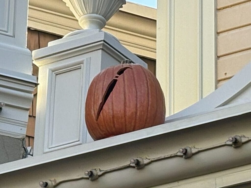 A Halloween decor Jack-o'-Lantern sits on a building ledge near ornate trim and fall-colored drapery.