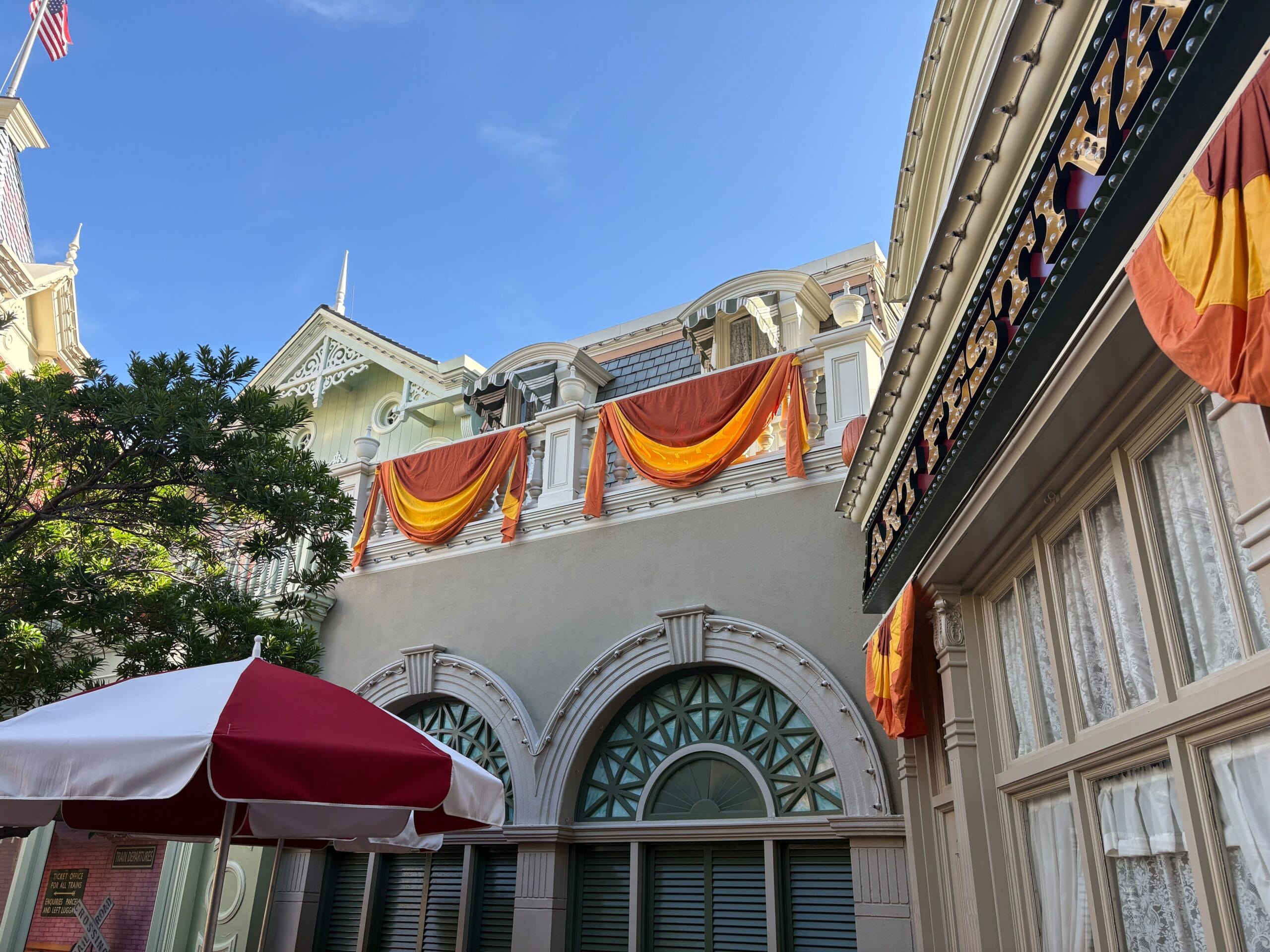 Orange and yellow Halloween decor hangs from balconies above arched windows, with a red-and-white umbrella in the foreground.