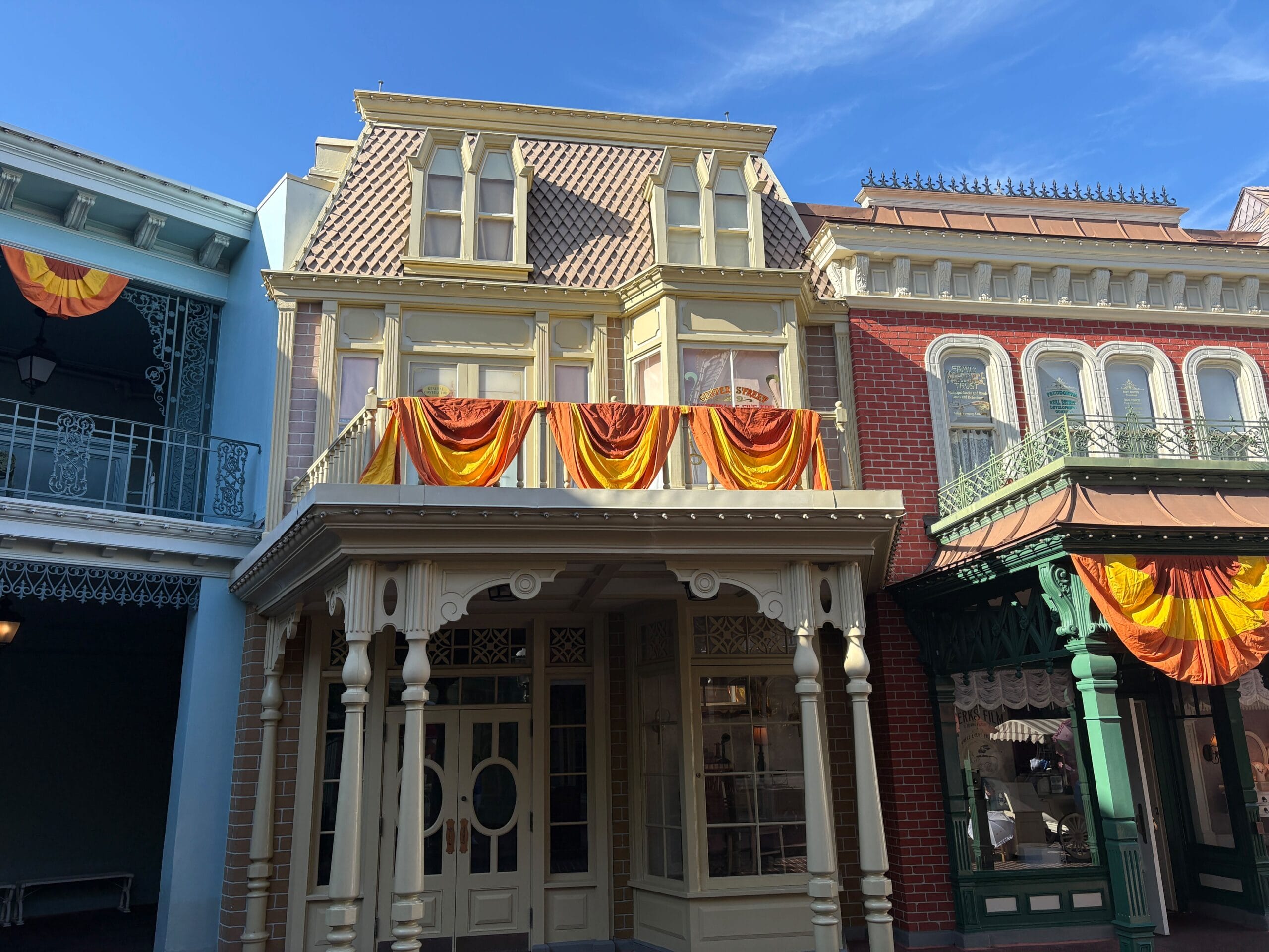 Two-story building with Halloween decor, wooden trim, and large windows near Magic Kingdom under a blue sky.