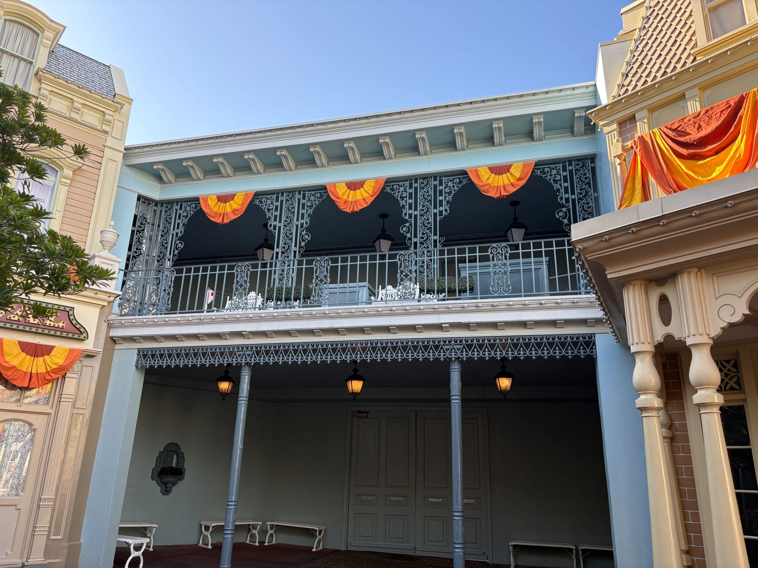 A building with Halloween decor and Jack-o'-Lanterns, orange bunting, and lights under a clear blue Magic Kingdom sky.