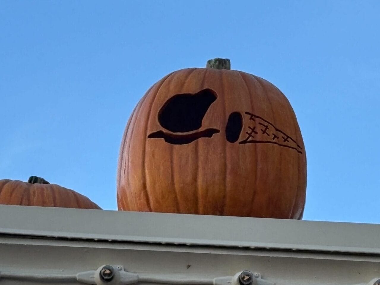 A Halloween Decor pumpkin with a witch hat and broom silhouette sits on a building ledge against a blue sky.