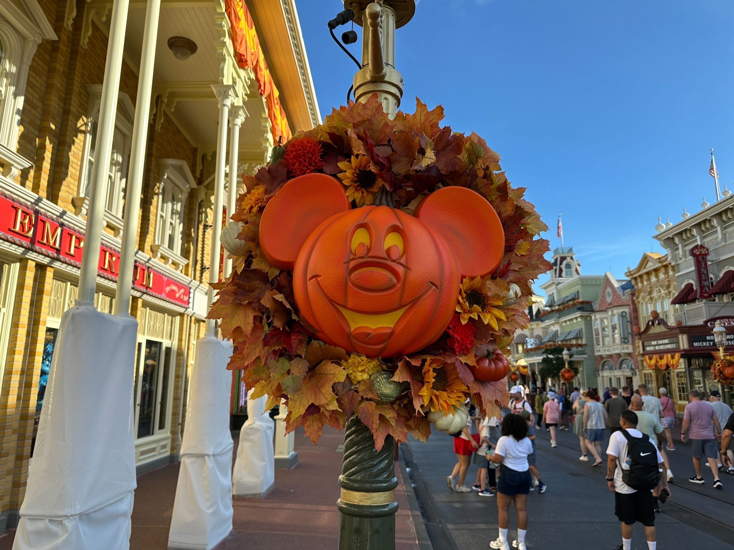 Mickey Jack-o'-Lantern Wreaths with autumn leaves decorate a lamppost on a busy Magic Kingdom street.
