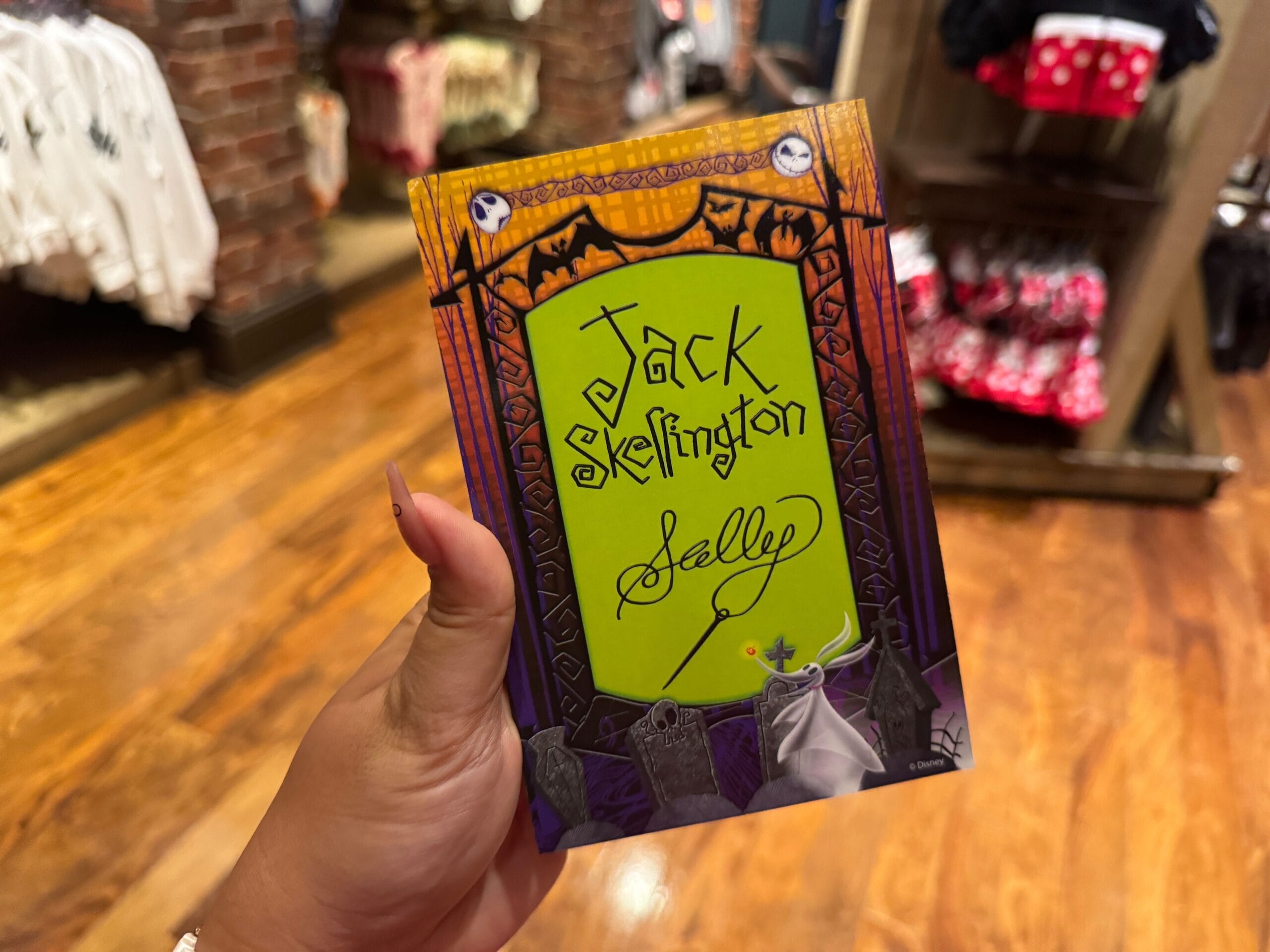 A hand holds a "Jack Skellington & Sally" card in a store, perfect for 2025 character appearances at Mickey's Not So Scary Halloween Party.