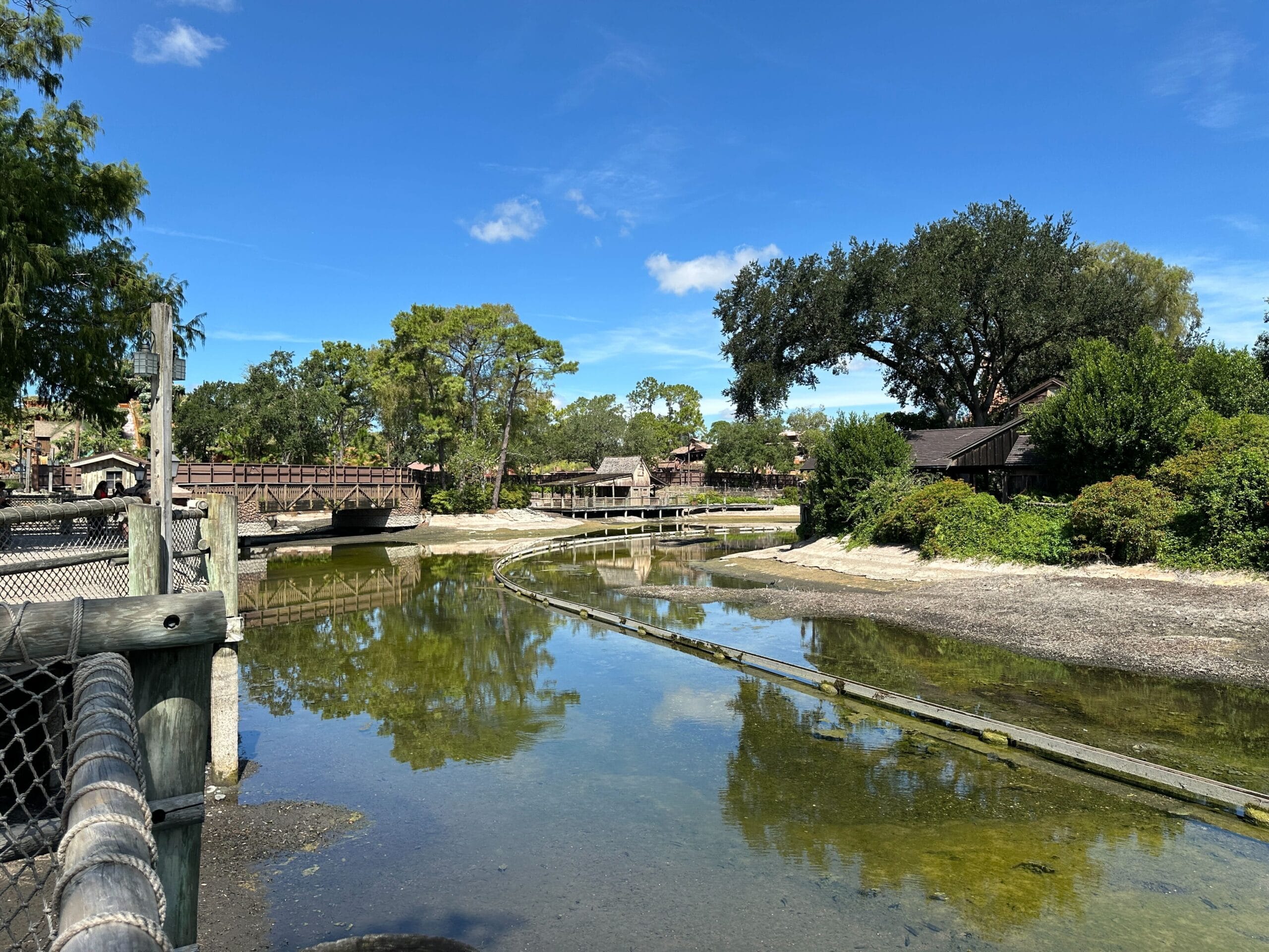 A shallow lagoon with a wooden fence, bridges, and trees under a clear blue sky.