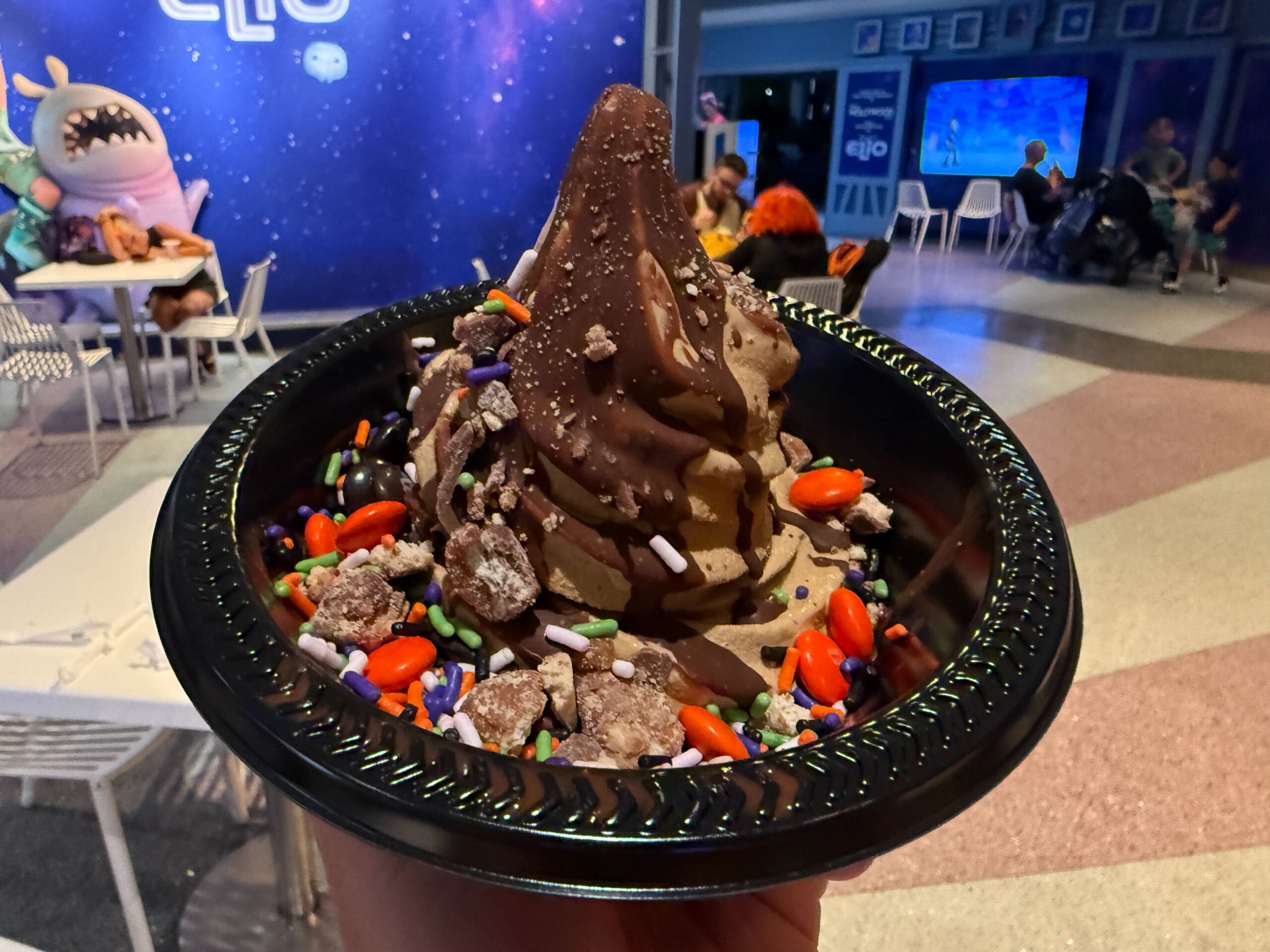A hand holds a bowl of chocolate soft serve with sprinkles and cookie crumbles at Mickey's Not So Scary Halloween Party.