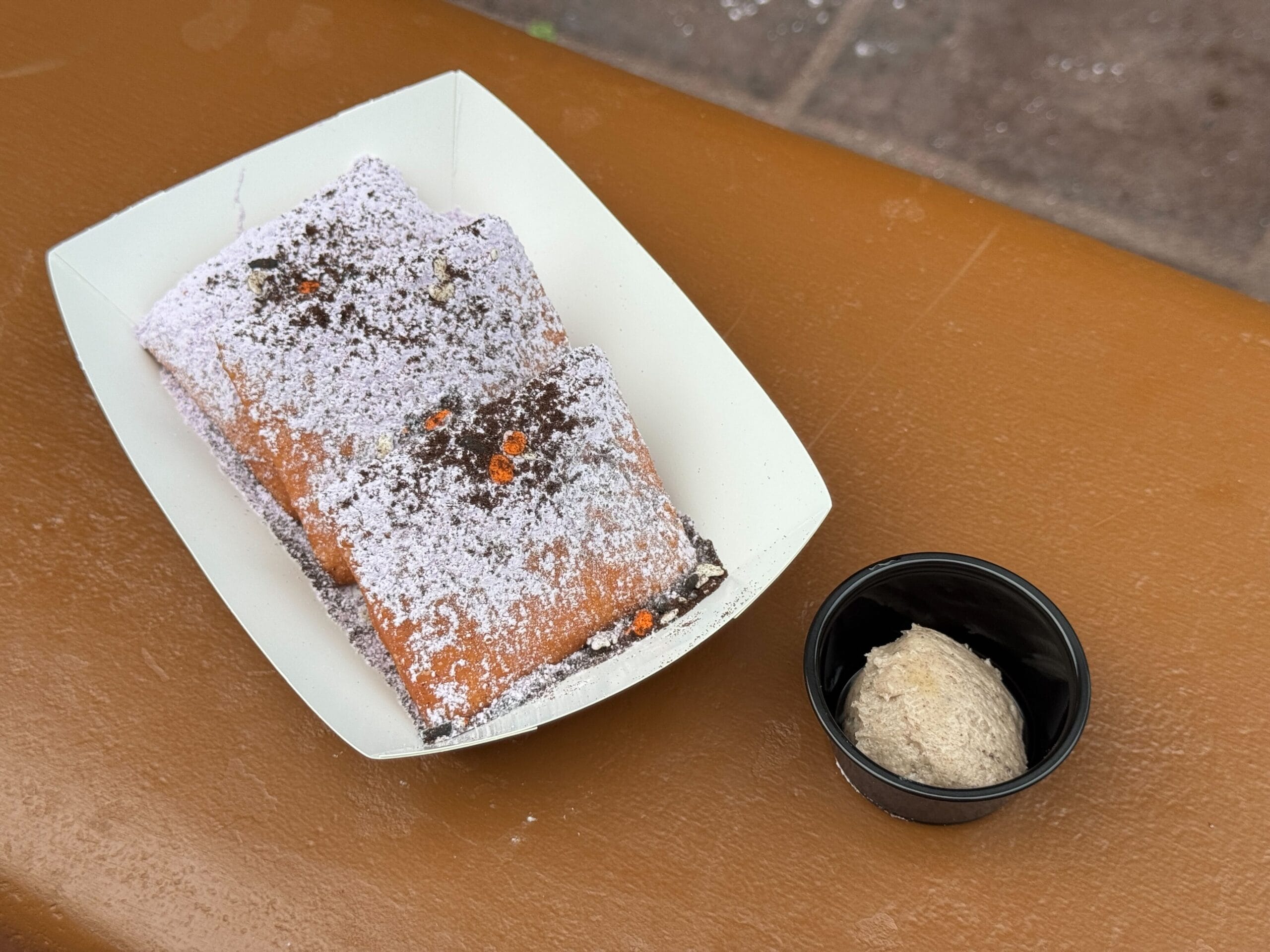 Two rectangular beignets dusted with powdered sugar, served at Mickey's Not So Scary Halloween Party with dipping sauce.