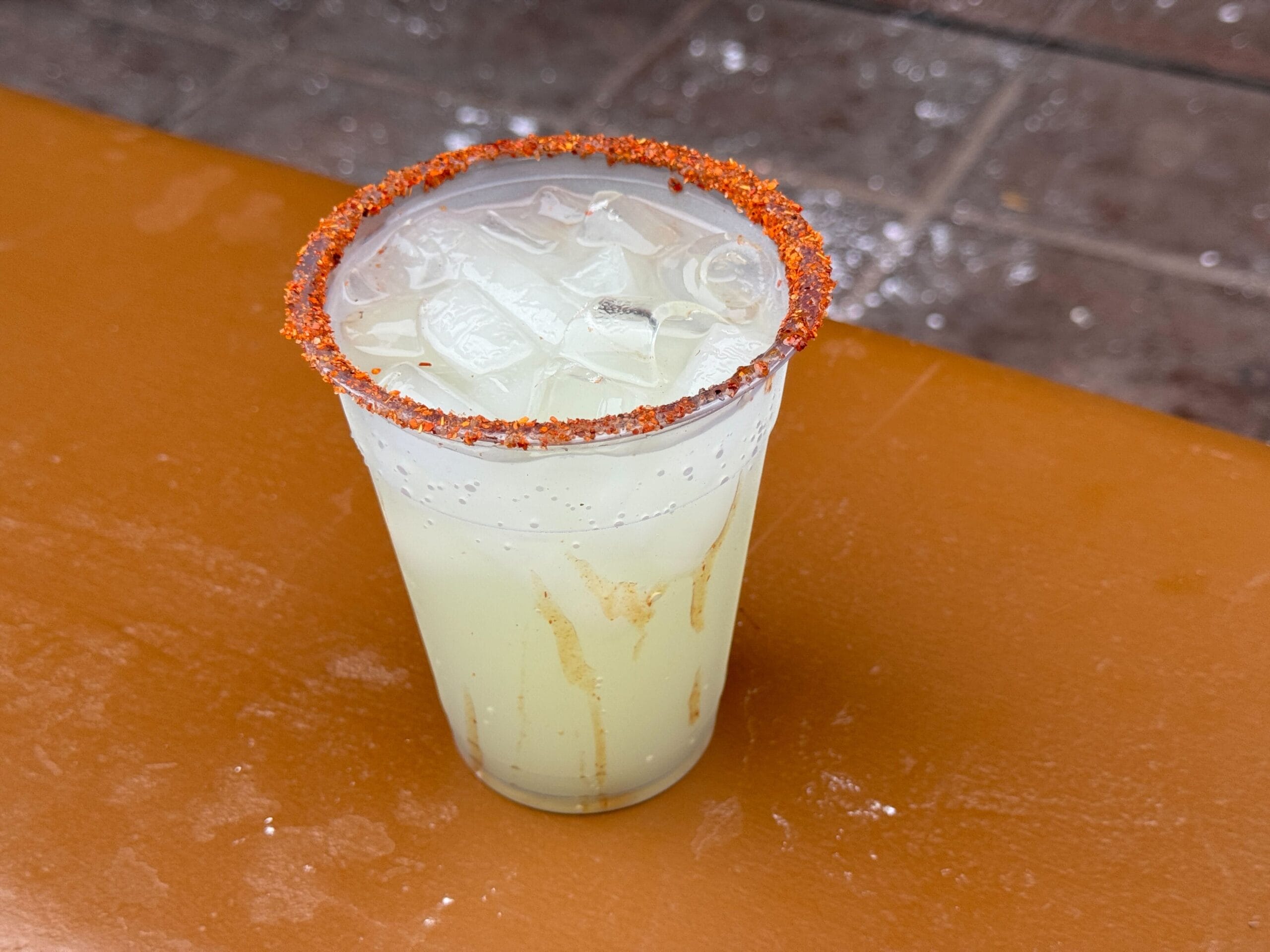 A plastic cup with chili powder rim, filled with iced yellow drink—perfect for food reviews at Mickey's Not So Scary Halloween Party.