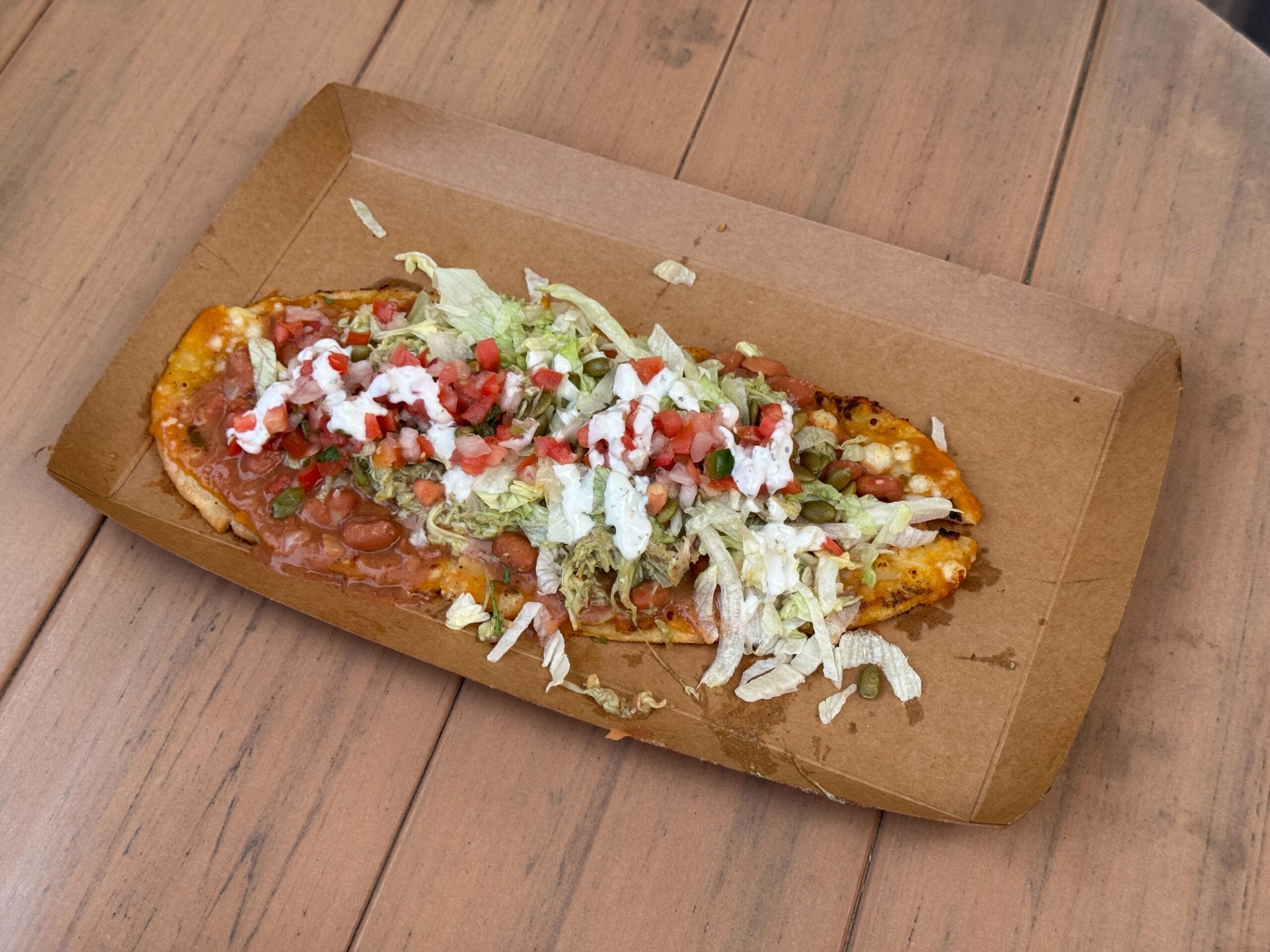 A flatbread topped with beans, lettuce, diced tomatoes, cheese, and sauces—perfect for food reviews on a wooden table.