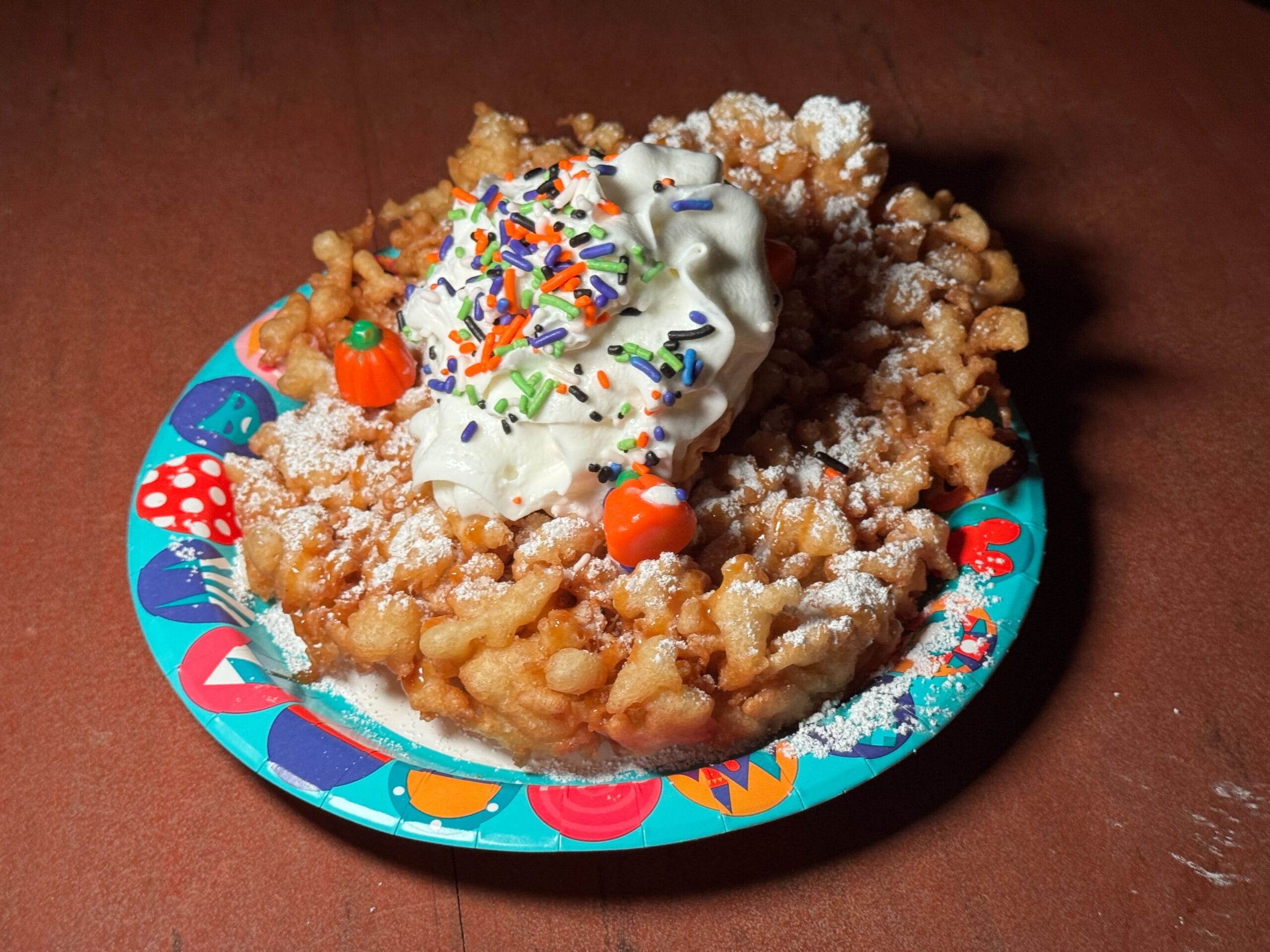 A funnel cake topped with whipped cream and candy pumpkins, perfect for Mickey's Not So Scary Halloween Party food reviews.