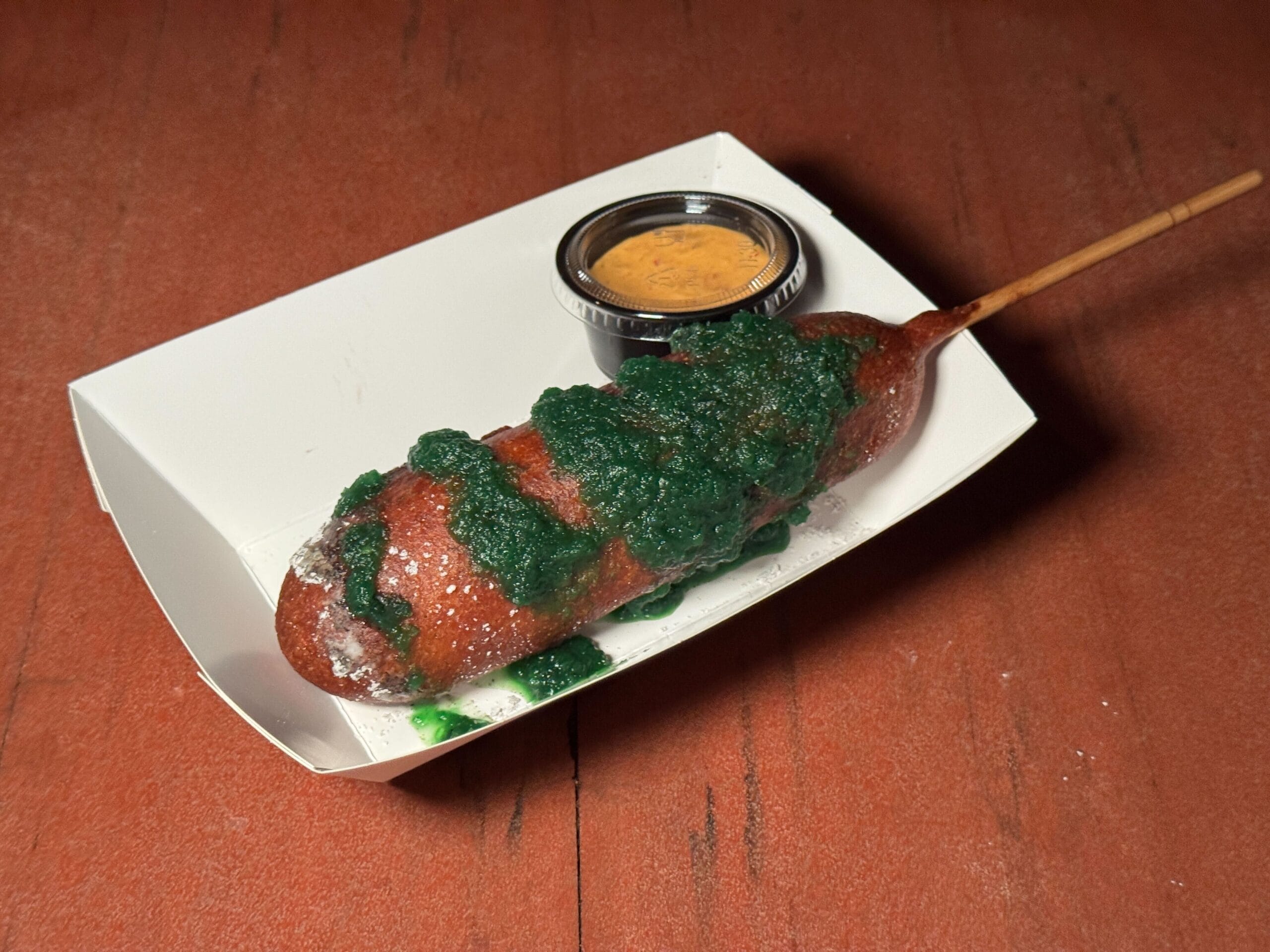 A corn dog with green sauce served tray-side, just like at Mickey's Not So Scary Halloween Party.