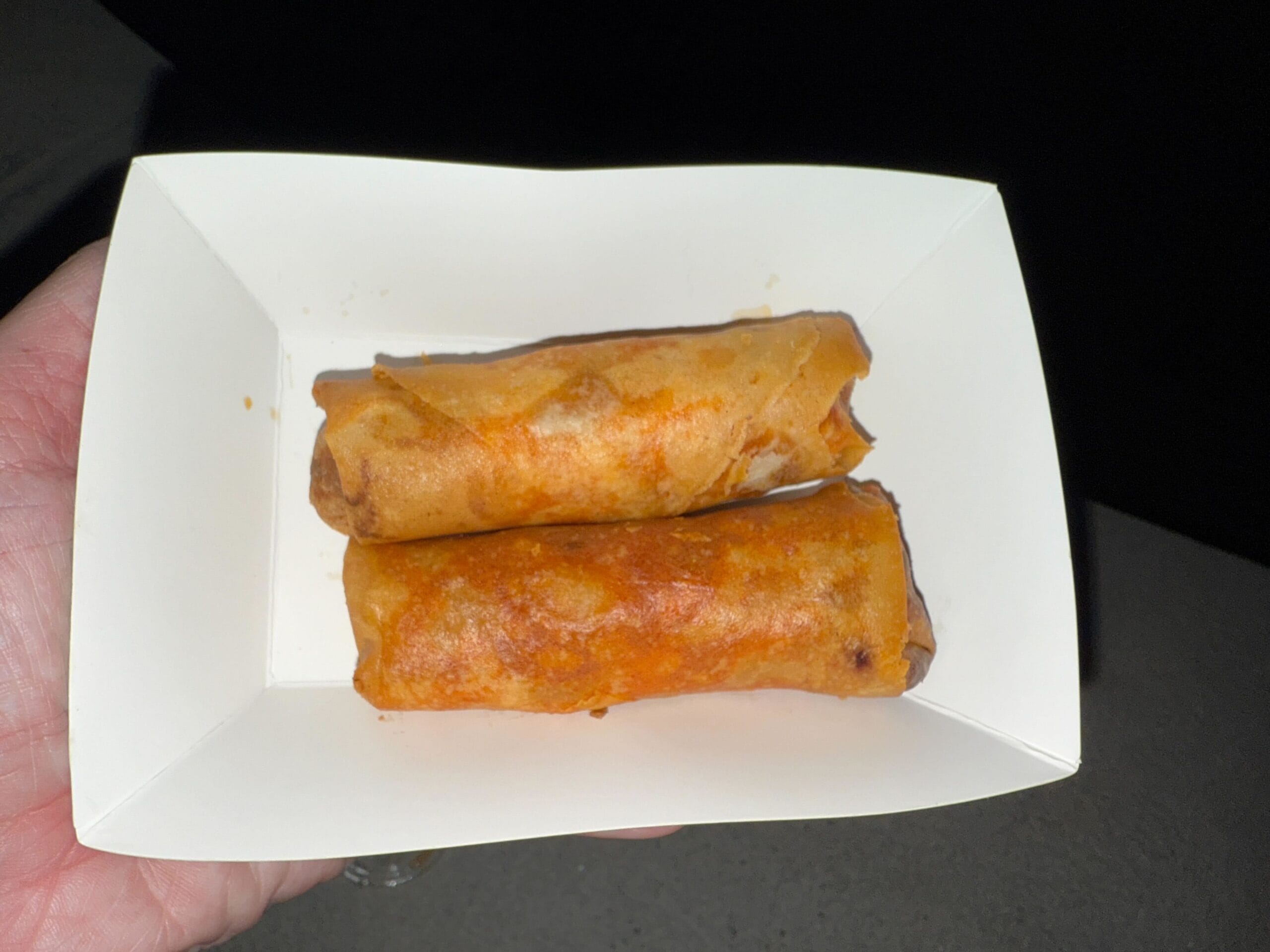 Two crispy spring rolls in a white paper tray, perfect for food reviews at Mickey's Not So Scary Halloween Party.