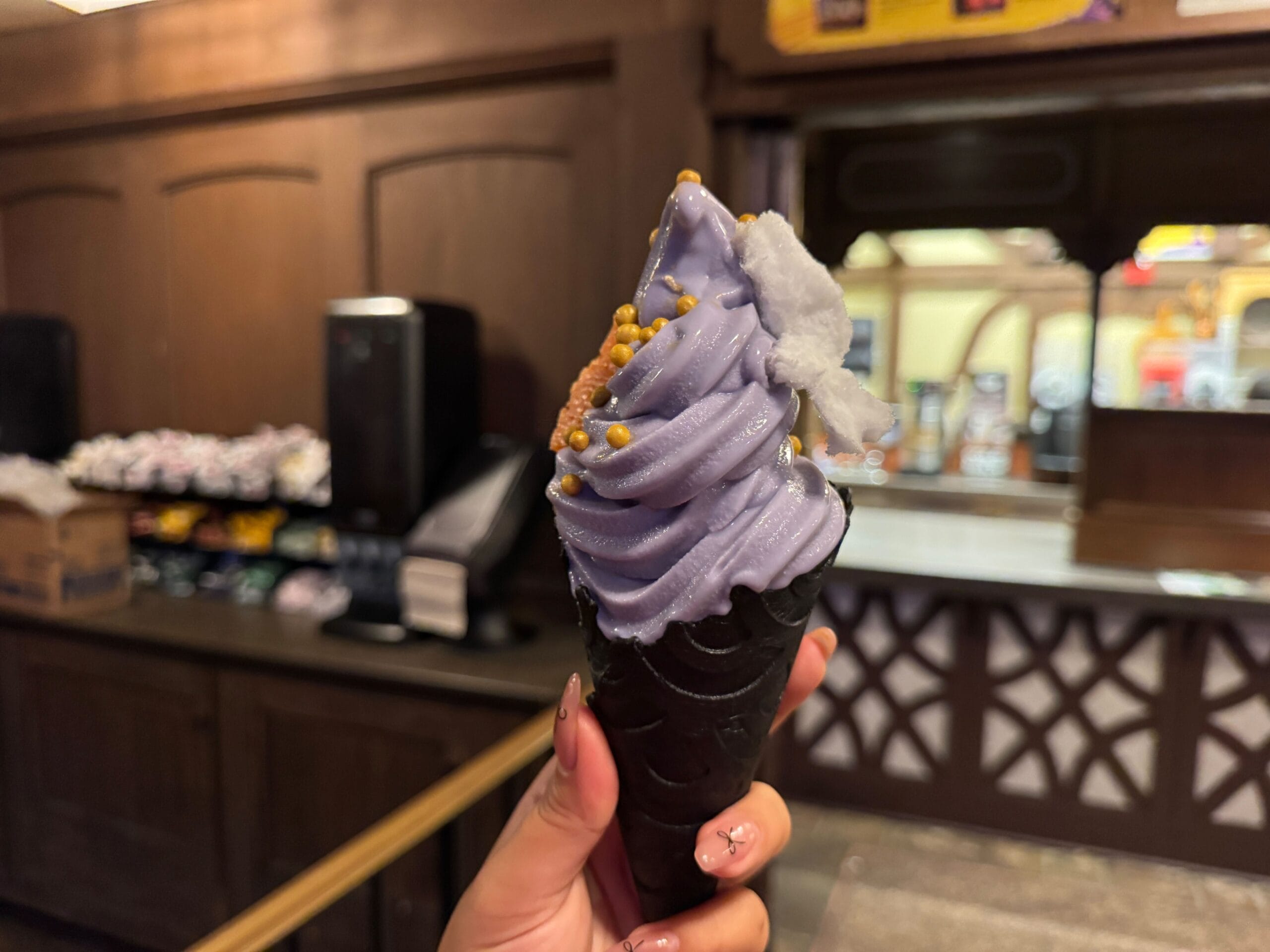 A hand holds a black cone with swirled purple soft serve—perfect for food reviews at Mickey's Not So Scary Halloween Party.