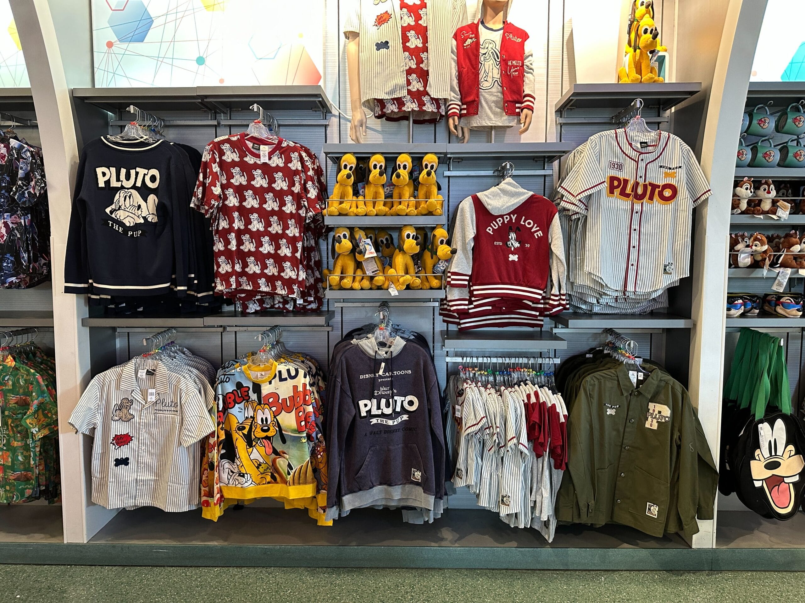 Sweaters, shirts, and Pluto plush toys from the Pluto Collection fill shelves in this Walt Disney World merchandise store.