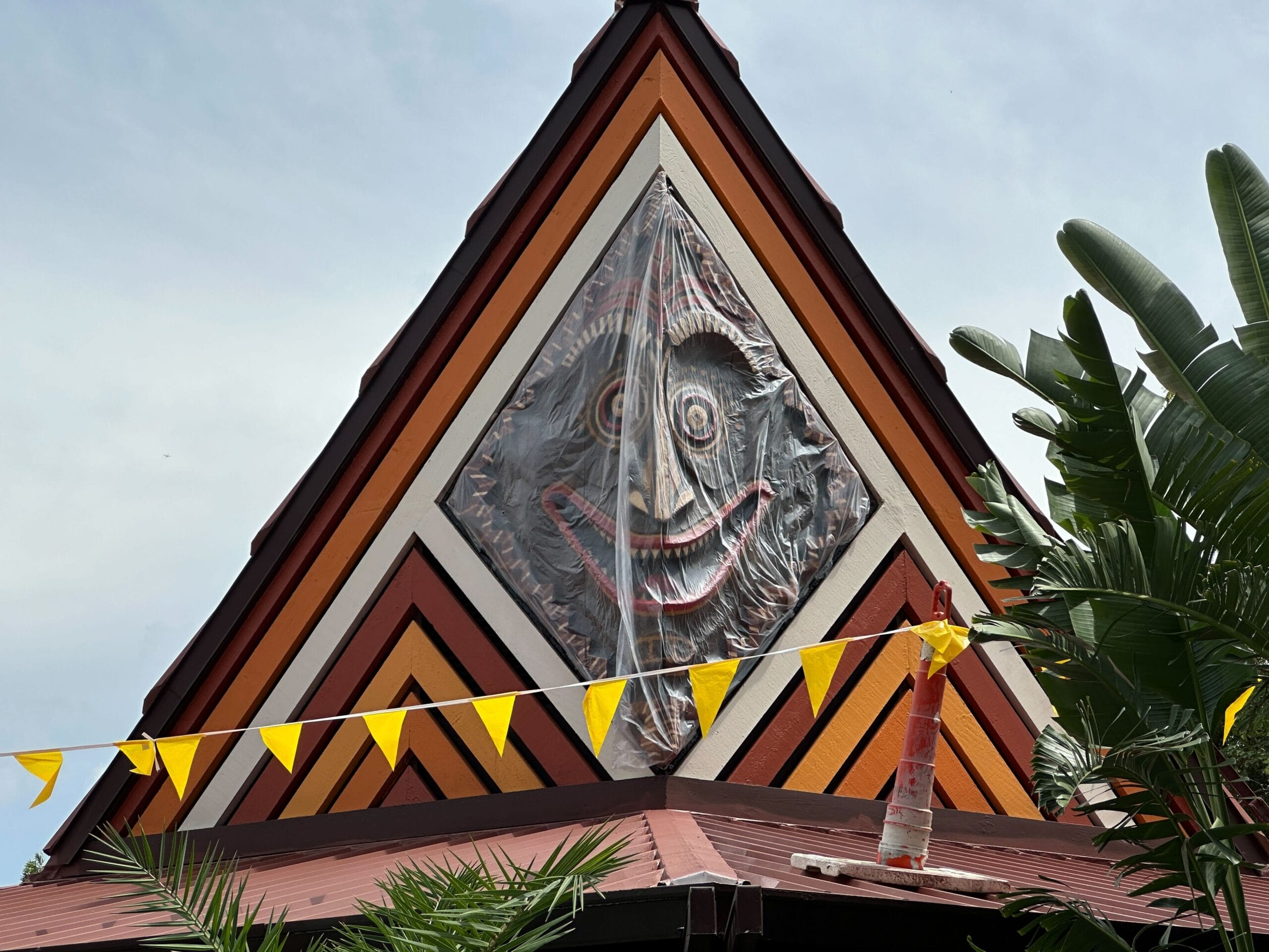 The peak of a building displays a large, colorful, smiling face covered in plastic, with yellow flags strung in front.